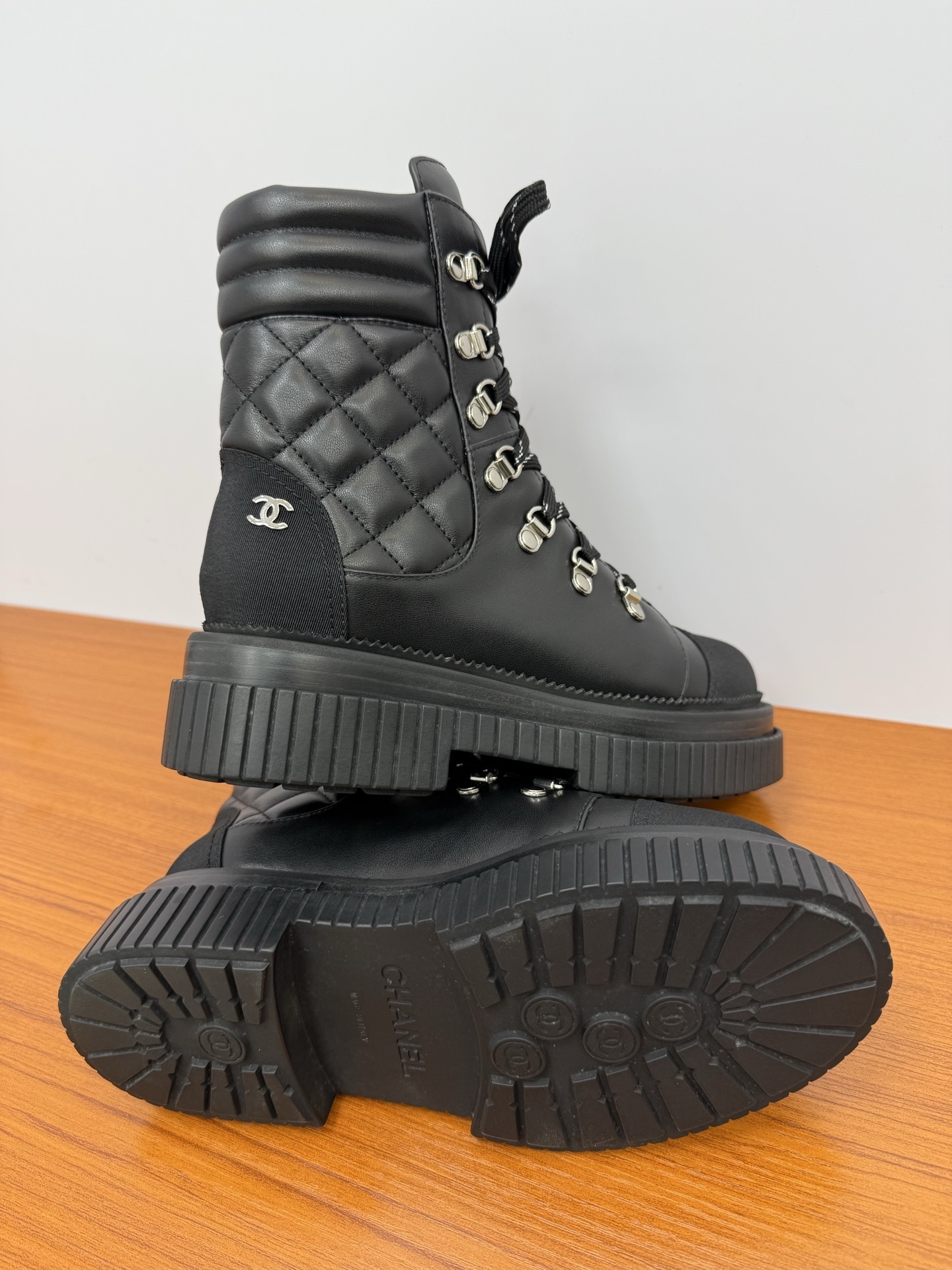 A pair of premium black quilted leather combat boots with chunky platform soles and patterned laces displayed on a wooden surface. - Hình 9