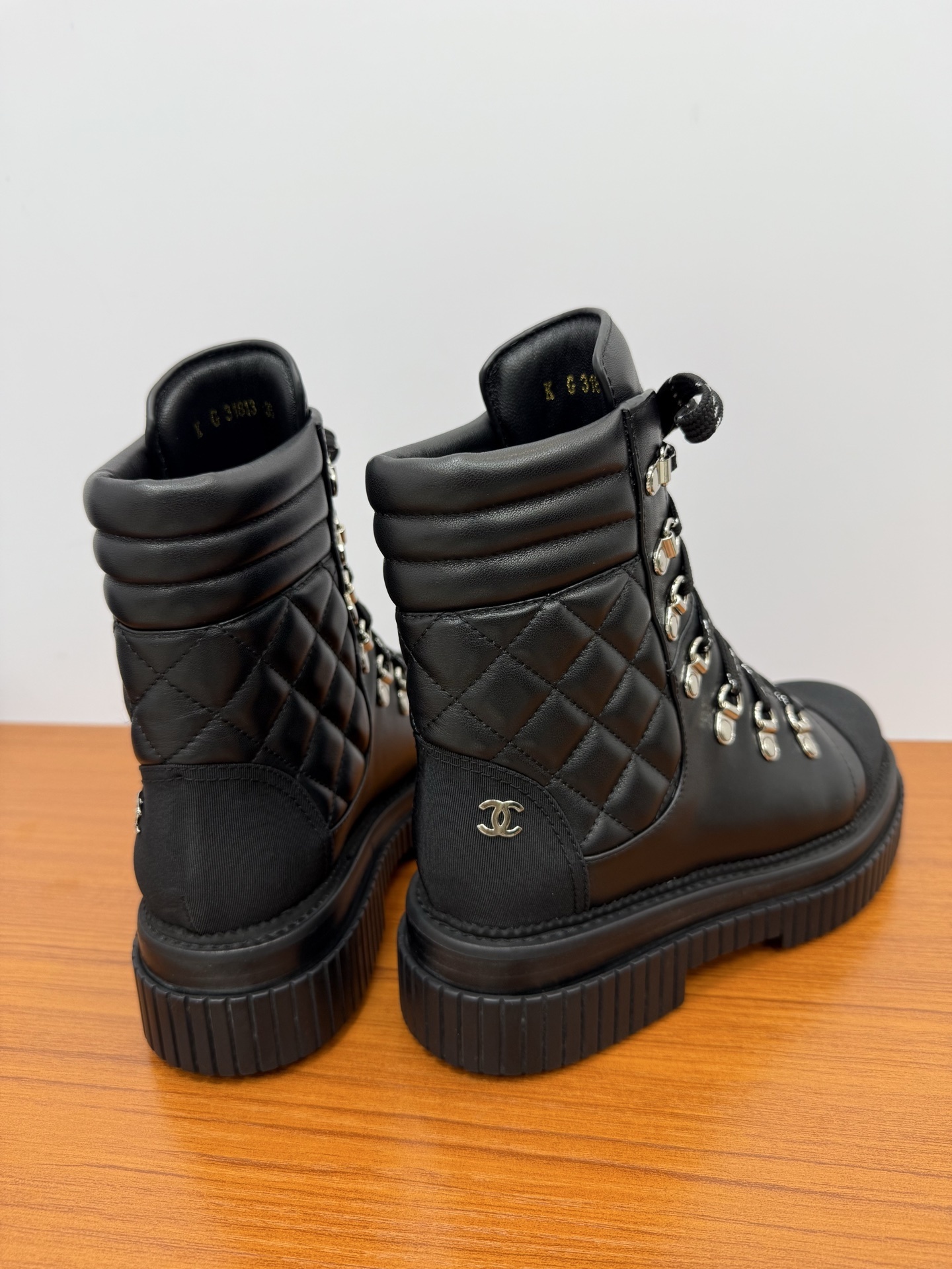 A pair of premium black quilted leather combat boots with chunky platform soles and patterned laces displayed on a wooden surface. - Hình 8