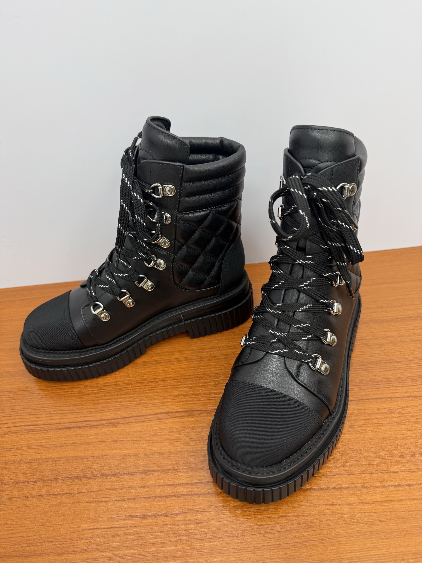 A pair of premium black quilted leather combat boots with chunky platform soles and patterned laces displayed on a wooden surface. - Hình 7