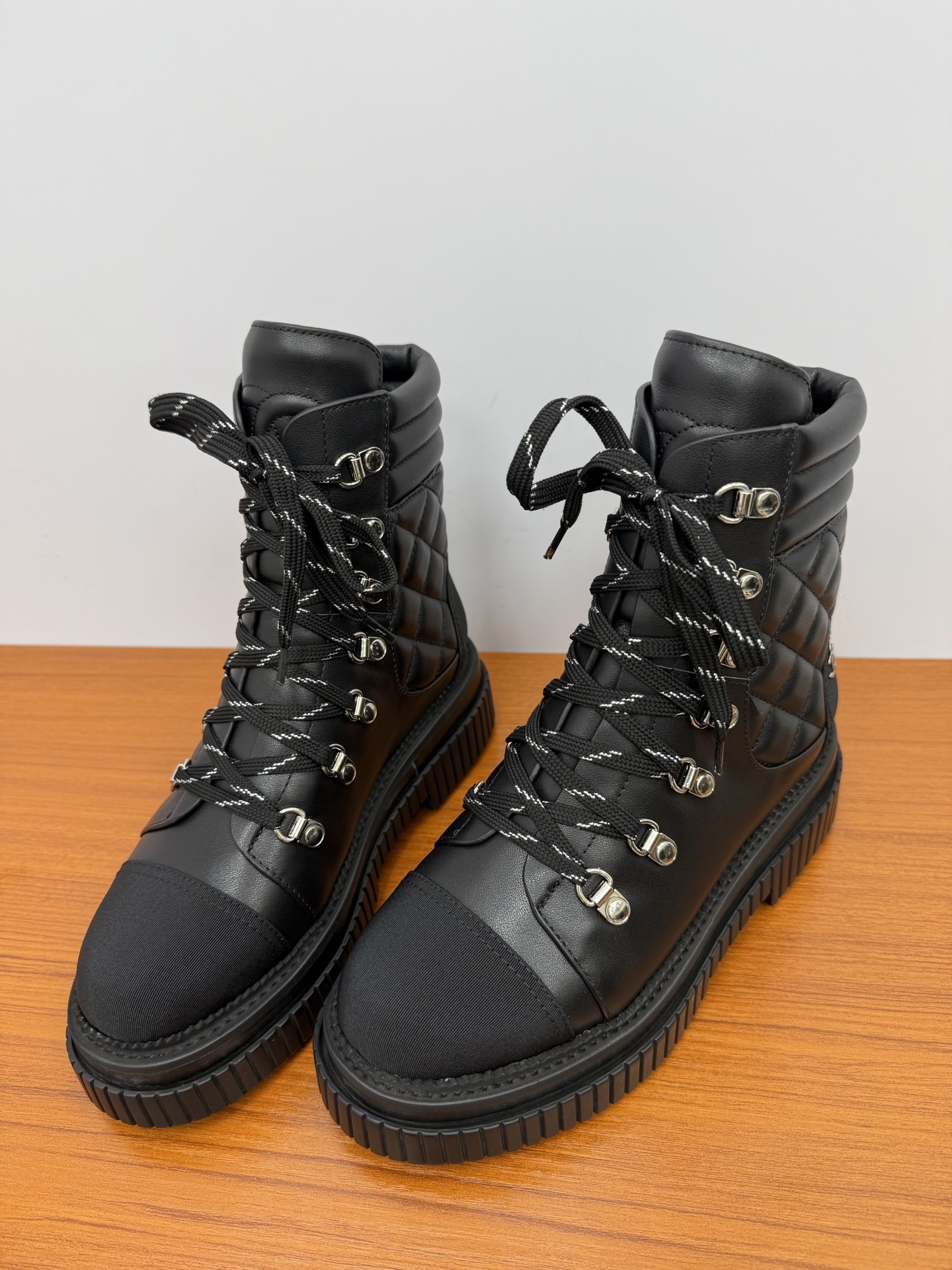 A pair of premium black quilted leather combat boots with chunky platform soles and patterned laces displayed on a wooden surface. - Hình 6