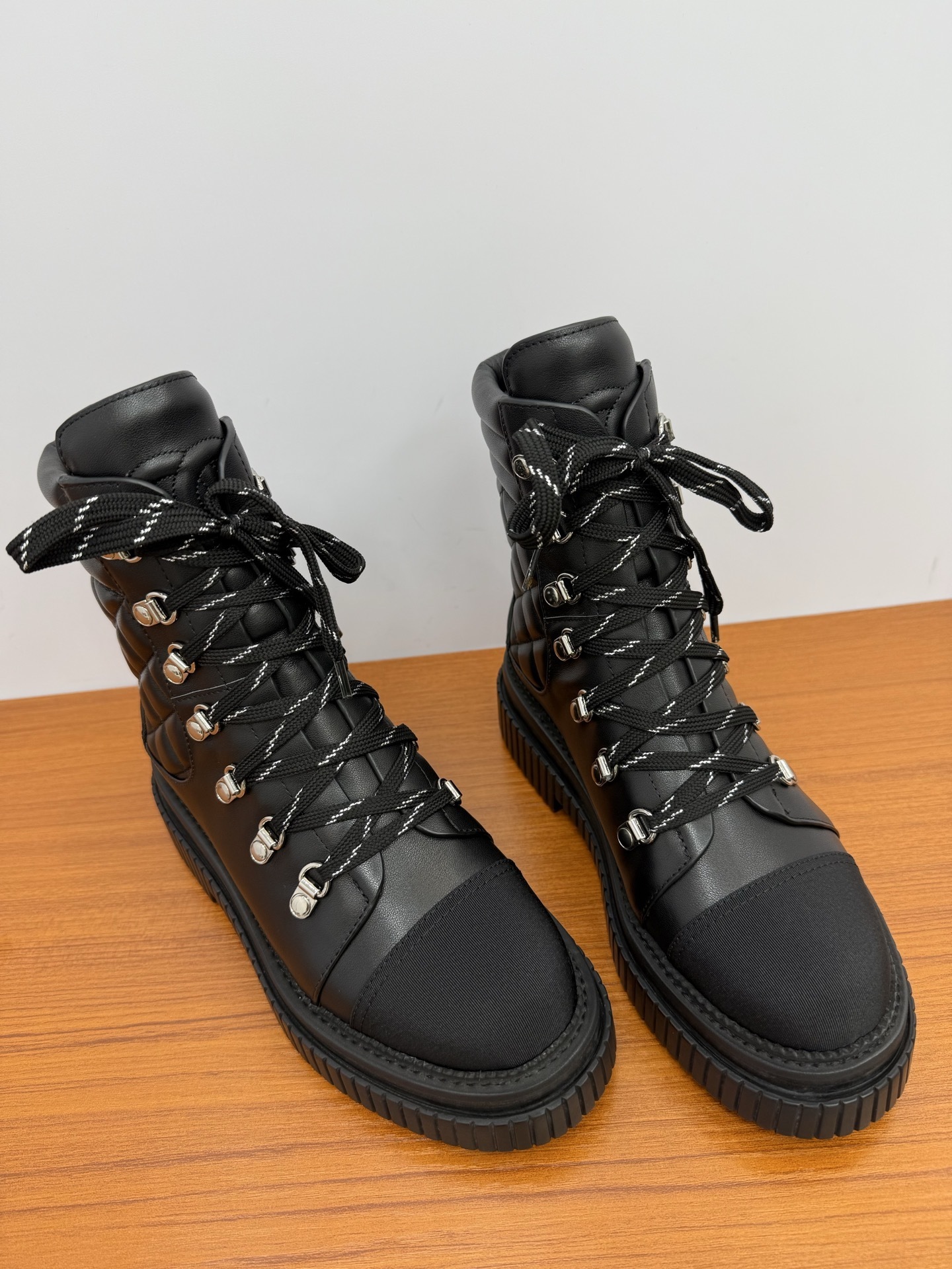 A pair of premium black quilted leather combat boots with chunky platform soles and patterned laces displayed on a wooden surface. - Hình 5
