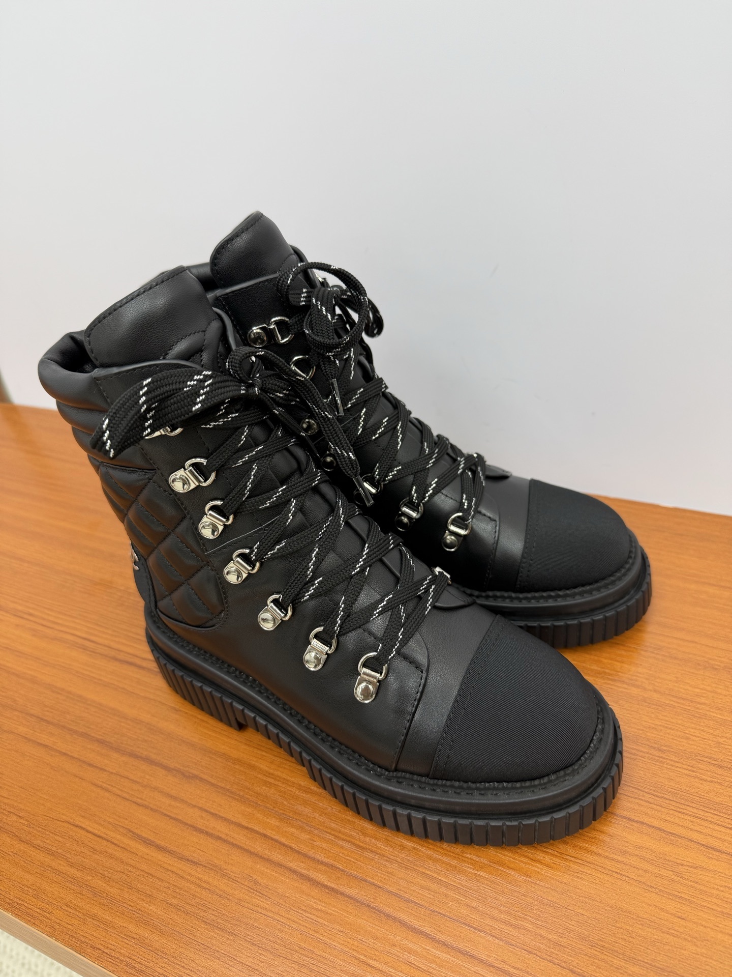 A pair of premium black quilted leather combat boots with chunky platform soles and patterned laces displayed on a wooden surface. - Hình 4
