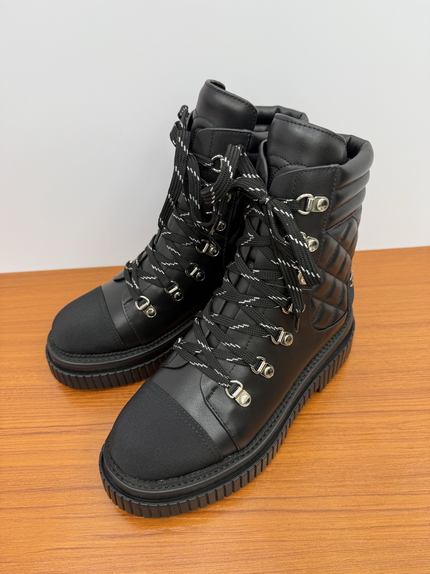 A pair of premium black quilted leather combat boots with chunky platform soles and patterned laces displayed on a wooden surface. - Hình 3