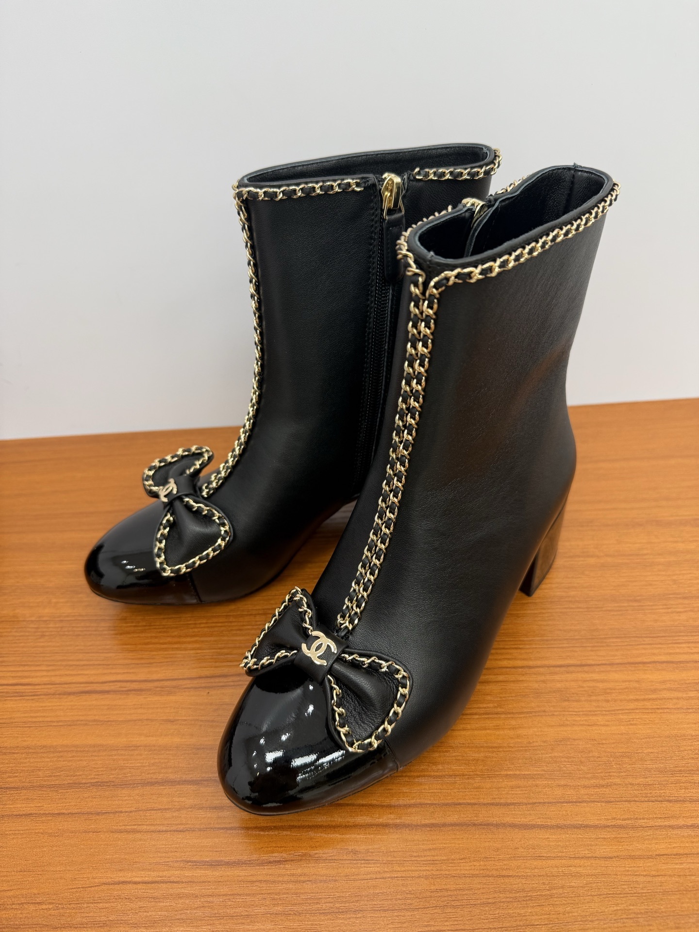 Pair of Chanel black leather ankle boots with patent toe caps, gold chain trim, and CC logo bows. - Hình 3