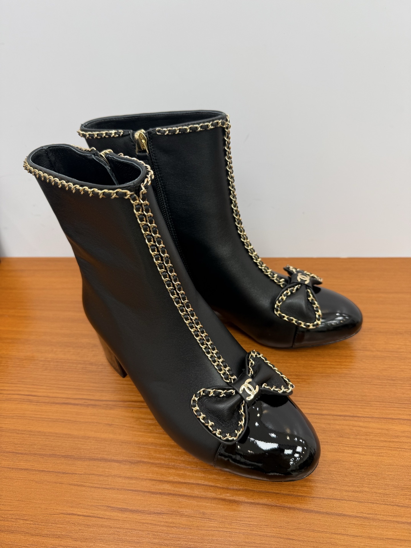 Pair of Chanel black leather ankle boots with patent toe caps, gold chain trim, and CC logo bows. - Hình 2