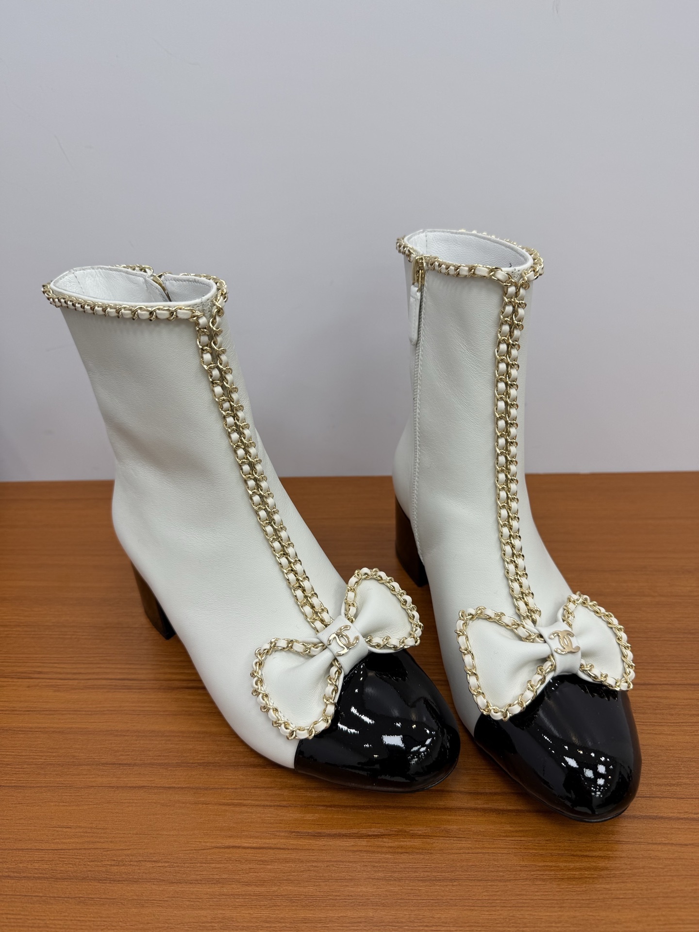 Elegant white leather ankle boots with black patent leather cap toe and gold chain trim with bow detail - Hình 5