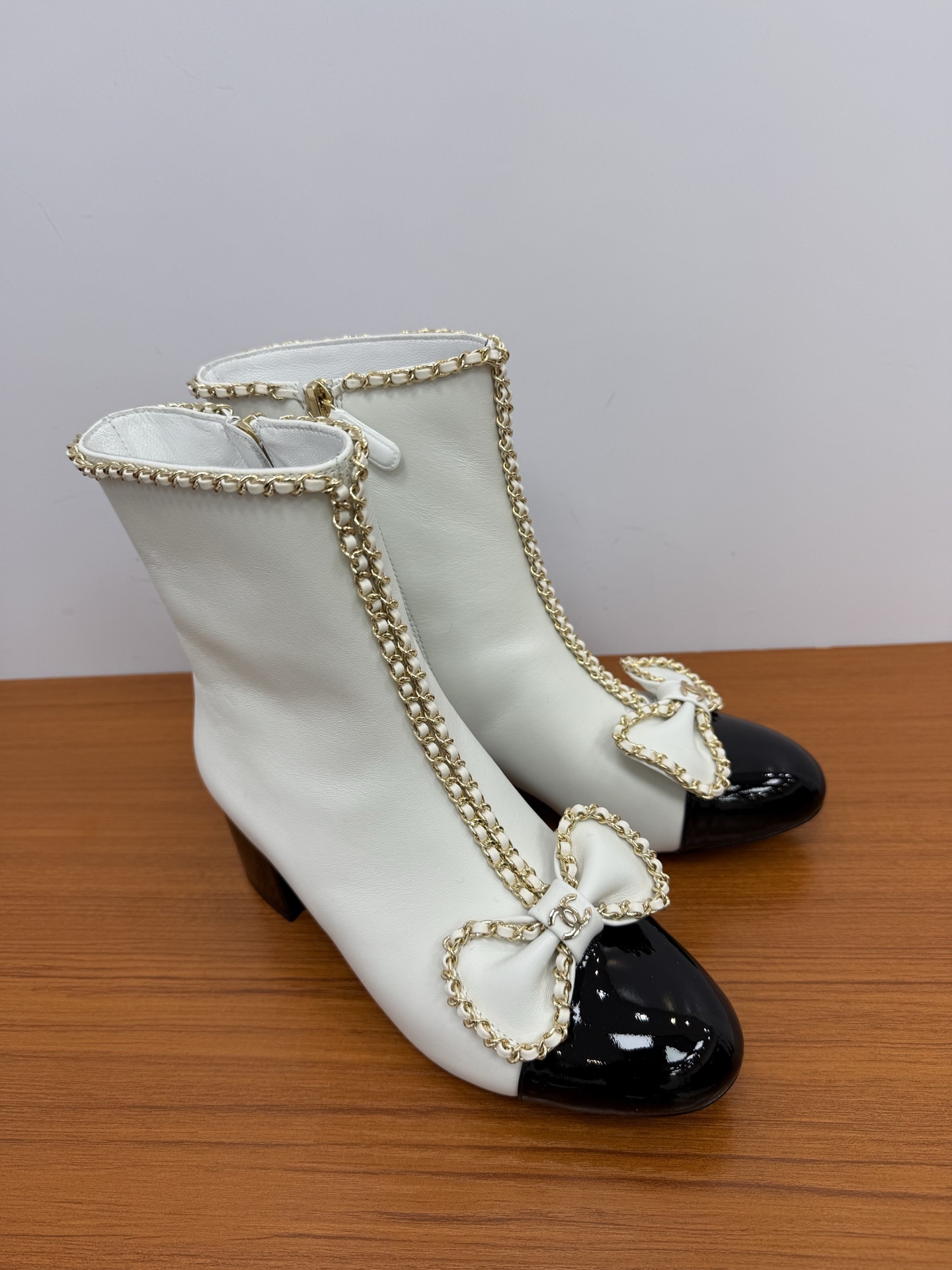 Elegant white leather ankle boots with black patent leather cap toe and gold chain trim with bow detail - Hình 2