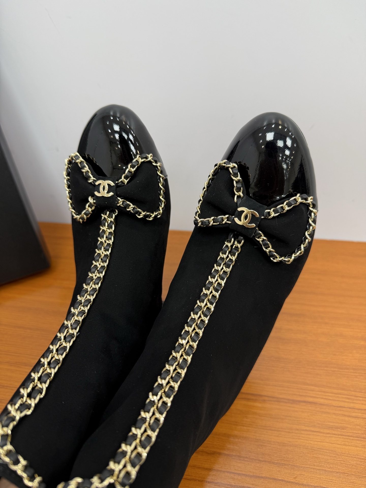 A pair of elegant black suede ankle boots with gold chain trim and a decorative bow on the patent leather toe cap. - Hình 9