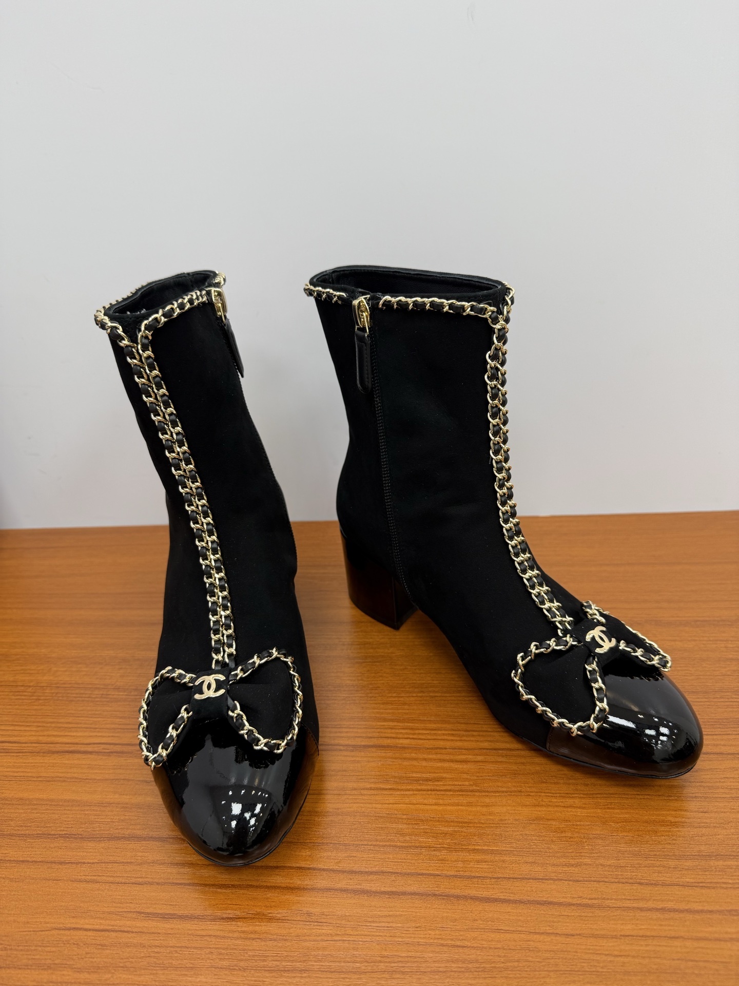A pair of elegant black suede ankle boots with gold chain trim and a decorative bow on the patent leather toe cap. - Hình 7