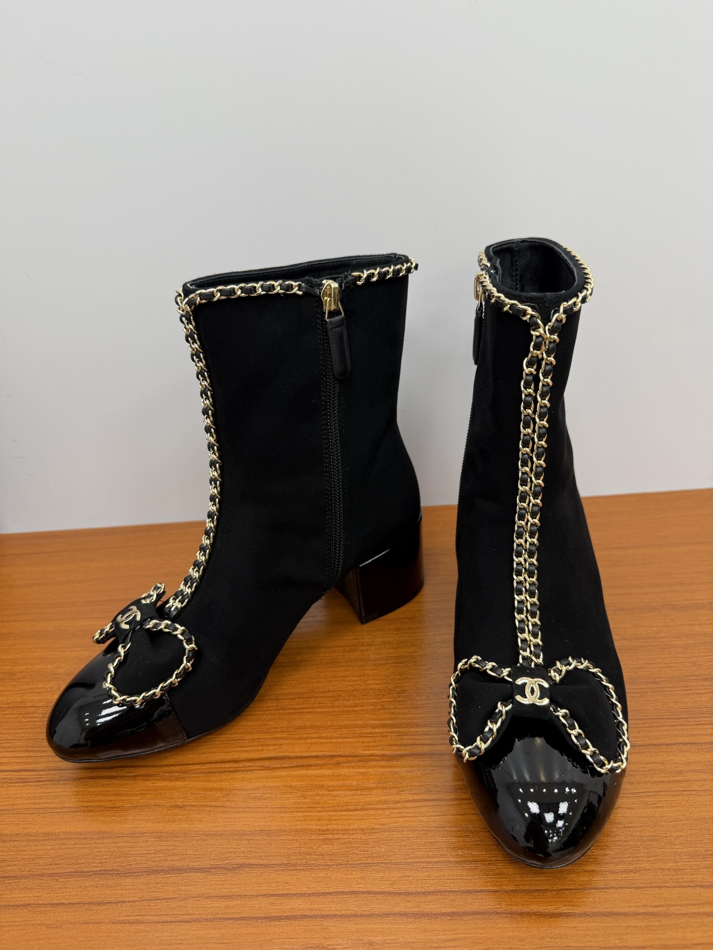 A pair of elegant black suede ankle boots with gold chain trim and a decorative bow on the patent leather toe cap. - Hình 6