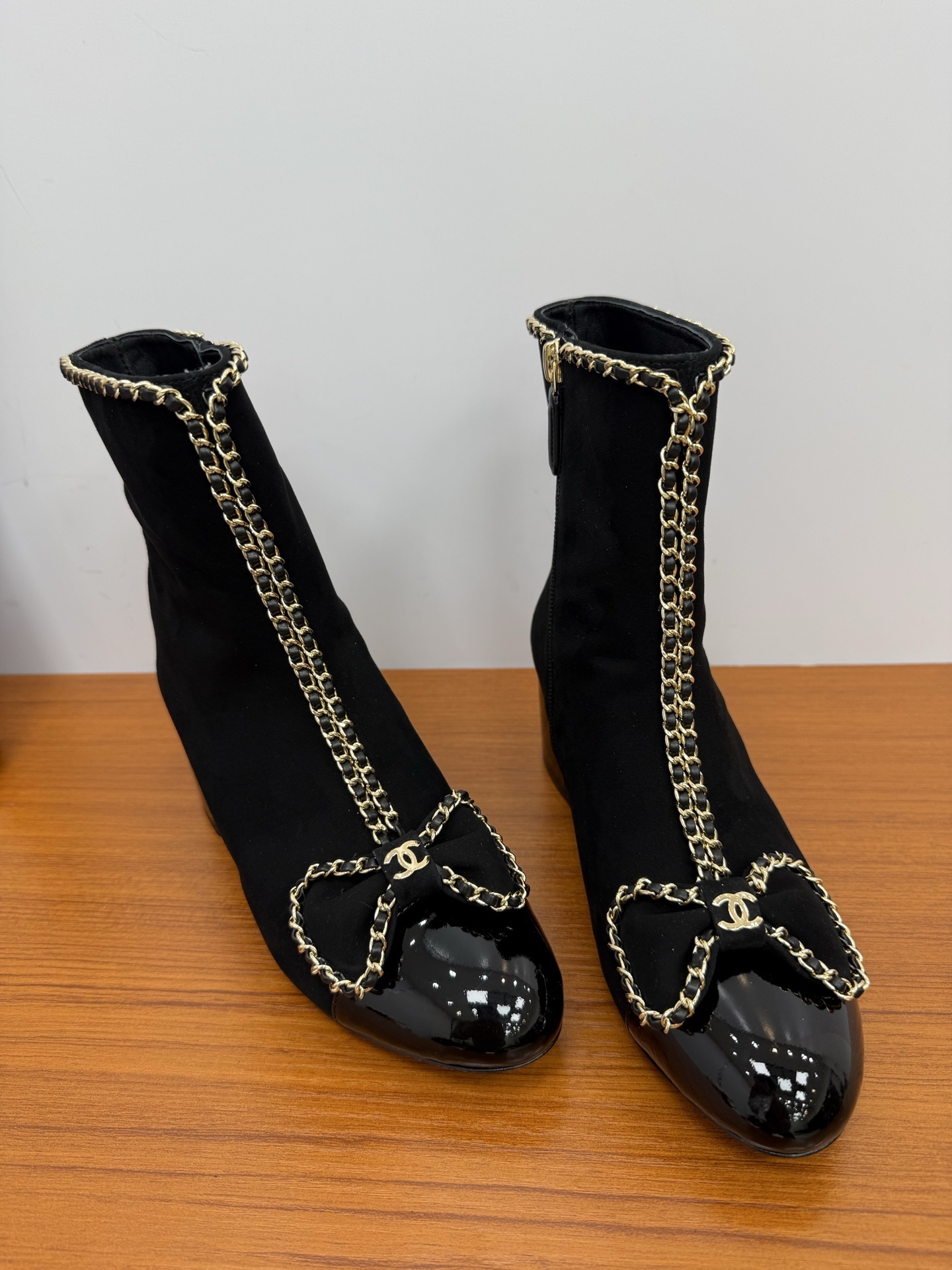 A pair of elegant black suede ankle boots with gold chain trim and a decorative bow on the patent leather toe cap. - Hình 4