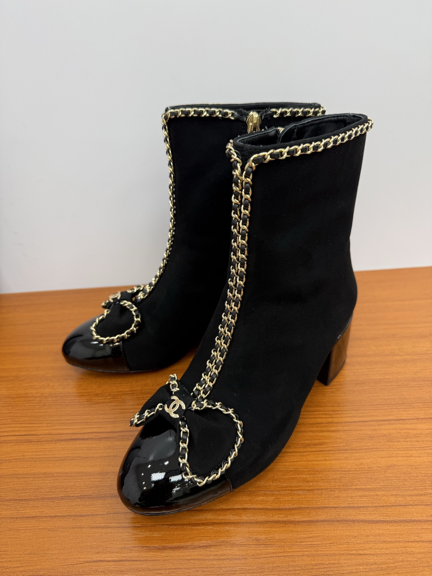 A pair of elegant black suede ankle boots with gold chain trim and a decorative bow on the patent leather toe cap. - Hình 3