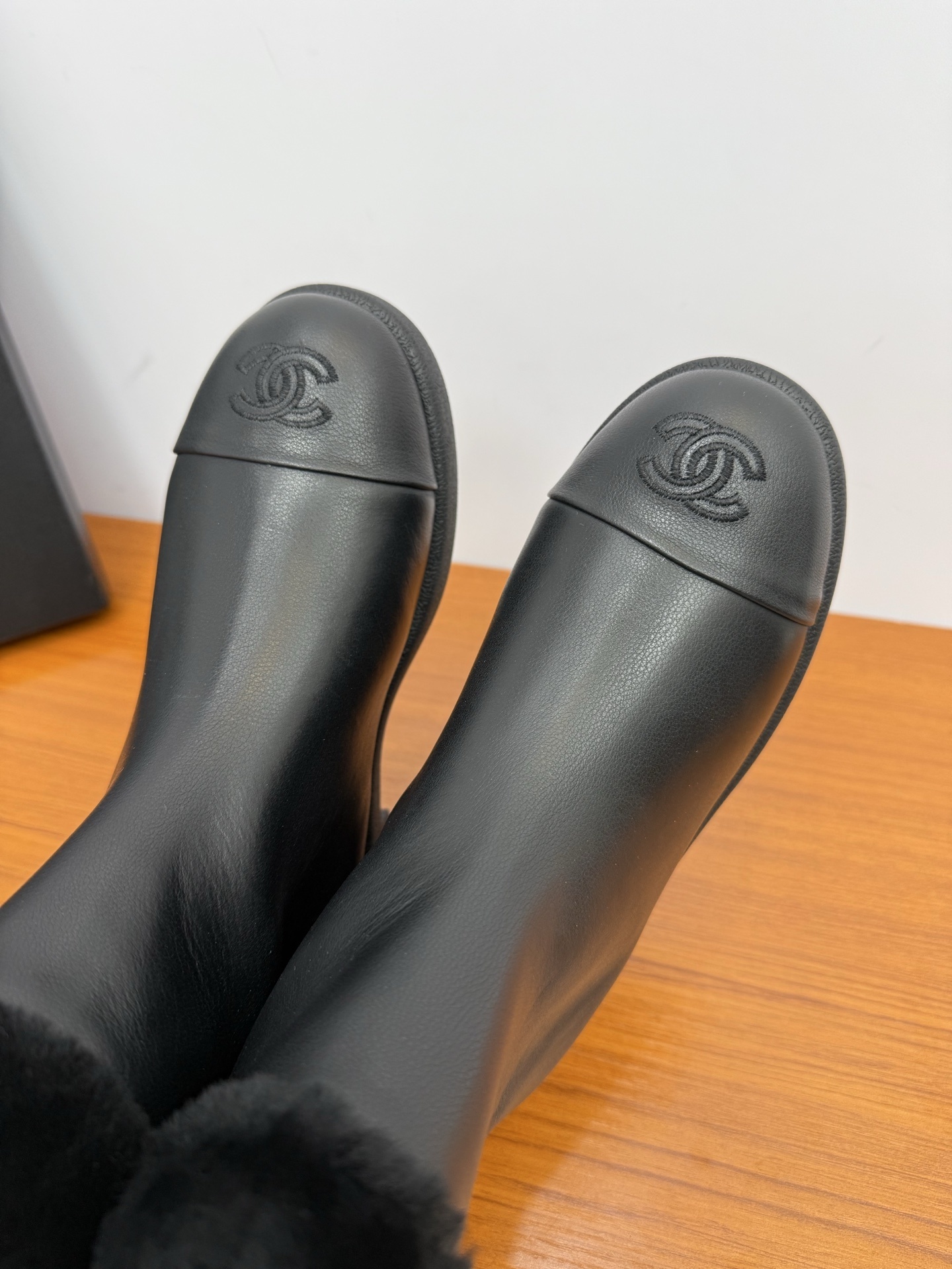 A pair of luxury Chanel black leather ankle boots featuring black fur trim at the collar and the embossed interlocking CC logo on the toe caps. - Hình 9