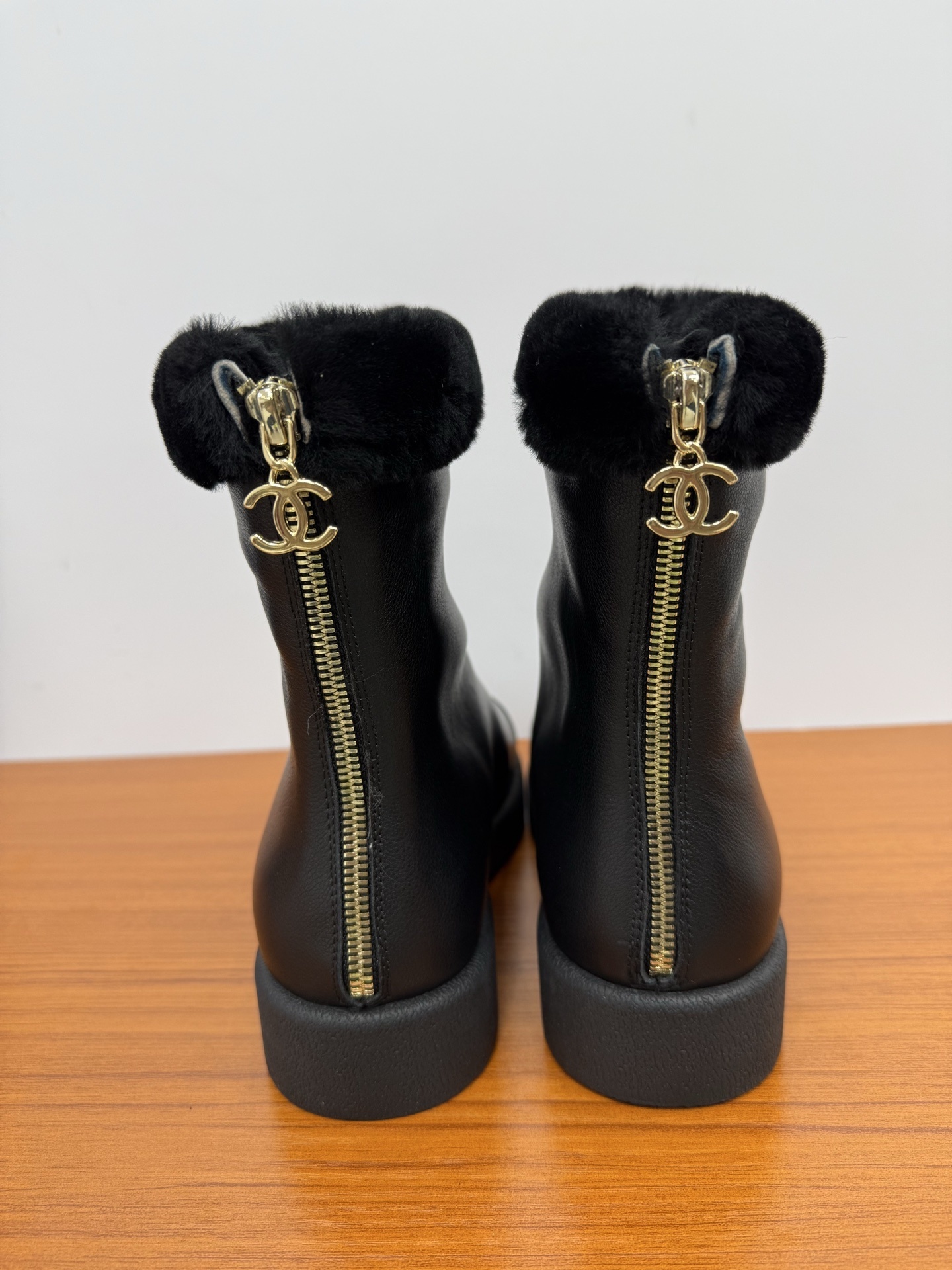 A pair of luxury Chanel black leather ankle boots featuring black fur trim at the collar and the embossed interlocking CC logo on the toe caps. - Hình 7