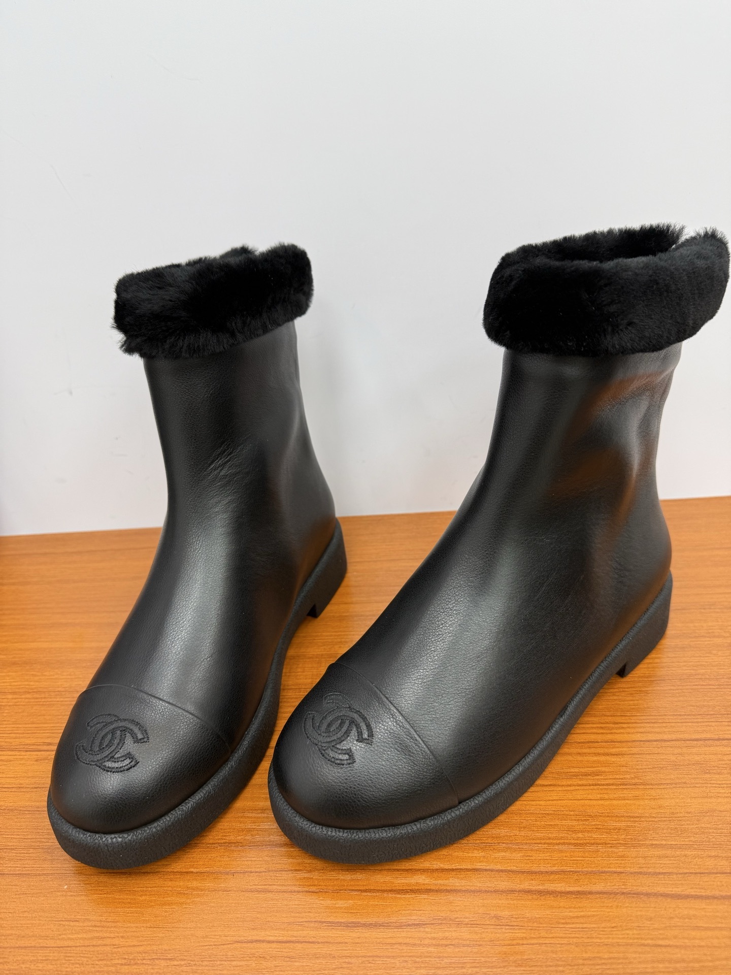 A pair of luxury Chanel black leather ankle boots featuring black fur trim at the collar and the embossed interlocking CC logo on the toe caps. - Hình 6