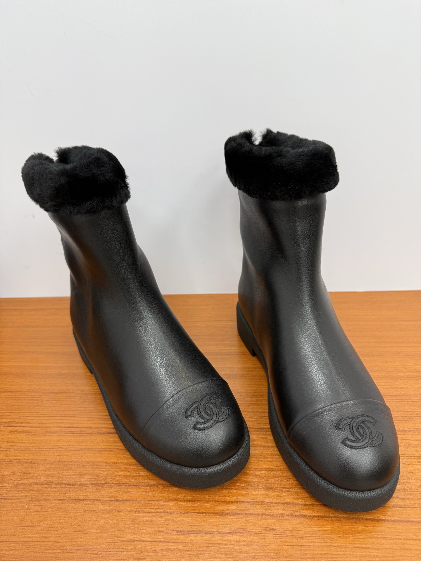 A pair of luxury Chanel black leather ankle boots featuring black fur trim at the collar and the embossed interlocking CC logo on the toe caps. - Hình 5