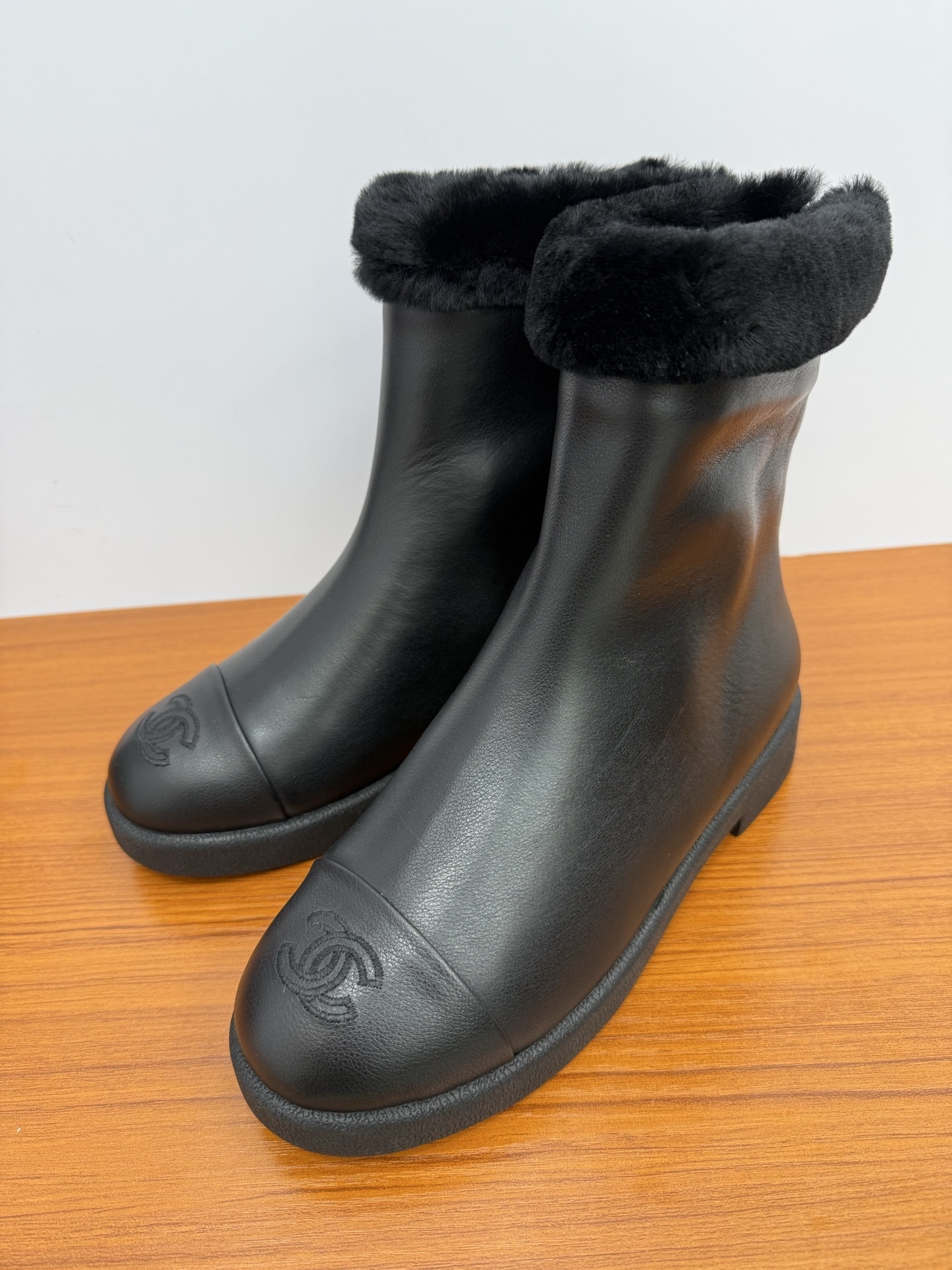 A pair of luxury Chanel black leather ankle boots featuring black fur trim at the collar and the embossed interlocking CC logo on the toe caps. - Hình 3