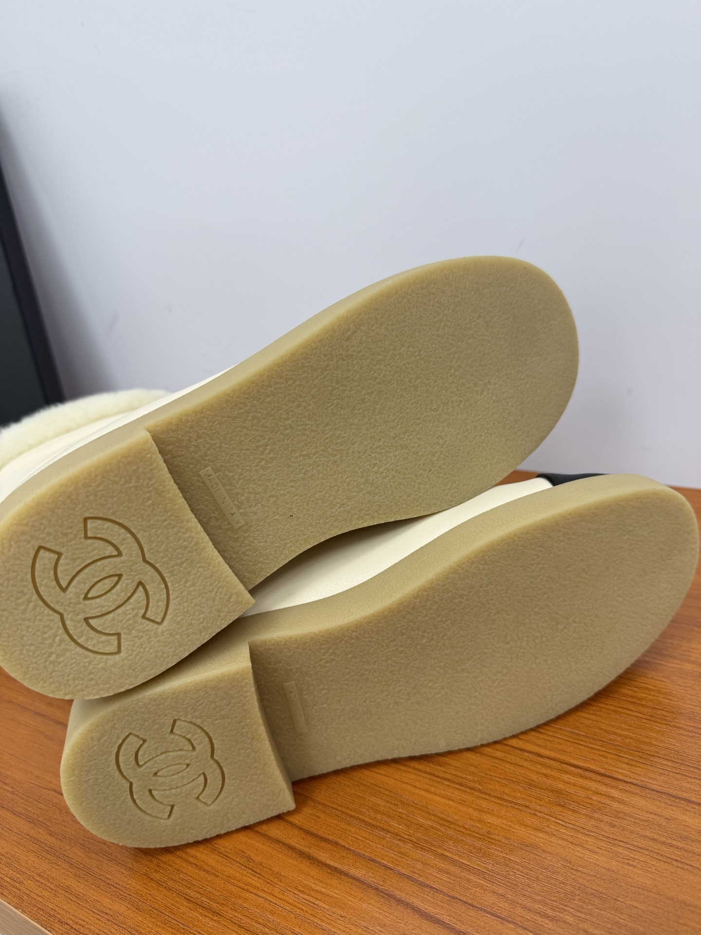 Pair of Chanel white leather ankle boots with black CC logo toe caps and white shearling trim on a wooden surface - Hình 8