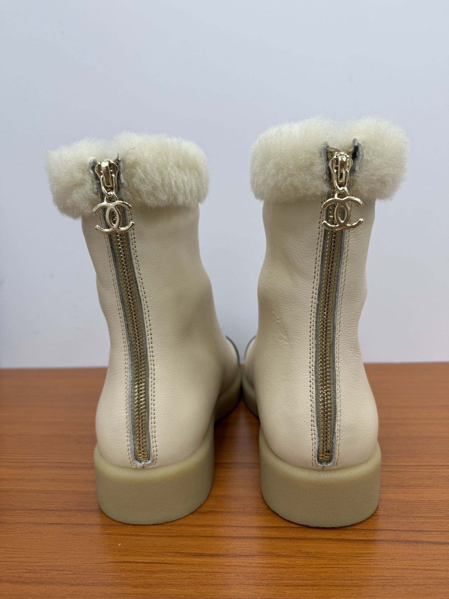 Pair of Chanel white leather ankle boots with black CC logo toe caps and white shearling trim on a wooden surface - Hình 7