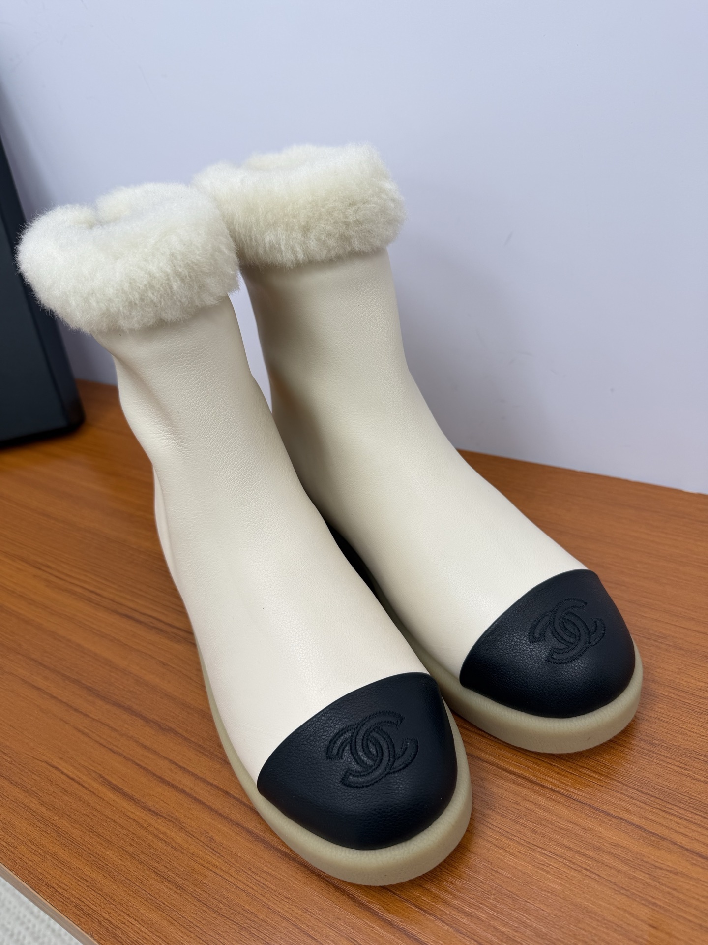 Pair of Chanel white leather ankle boots with black CC logo toe caps and white shearling trim on a wooden surface - Hình 4