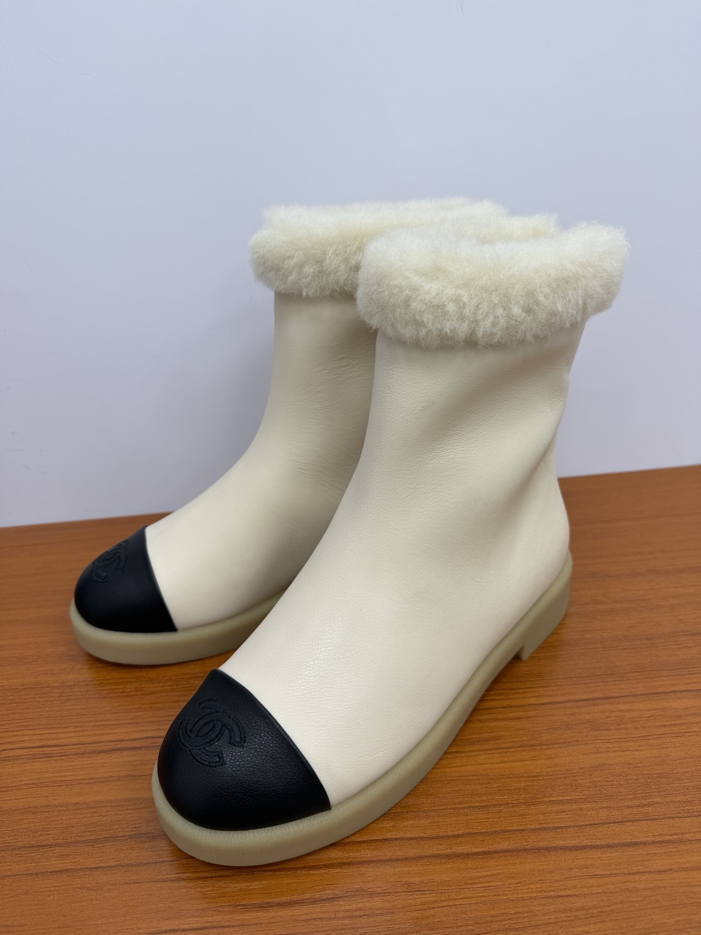 Pair of Chanel white leather ankle boots with black CC logo toe caps and white shearling trim on a wooden surface - Hình 3
