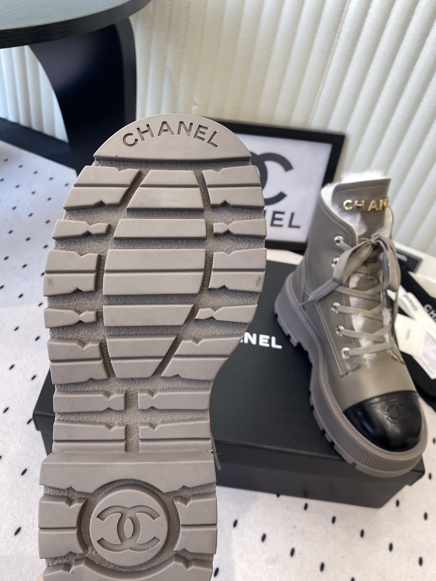 Chanel taupe leather lace-up boots with black patent toe caps and white shearling lining displayed on a black designer box - Hình 9
