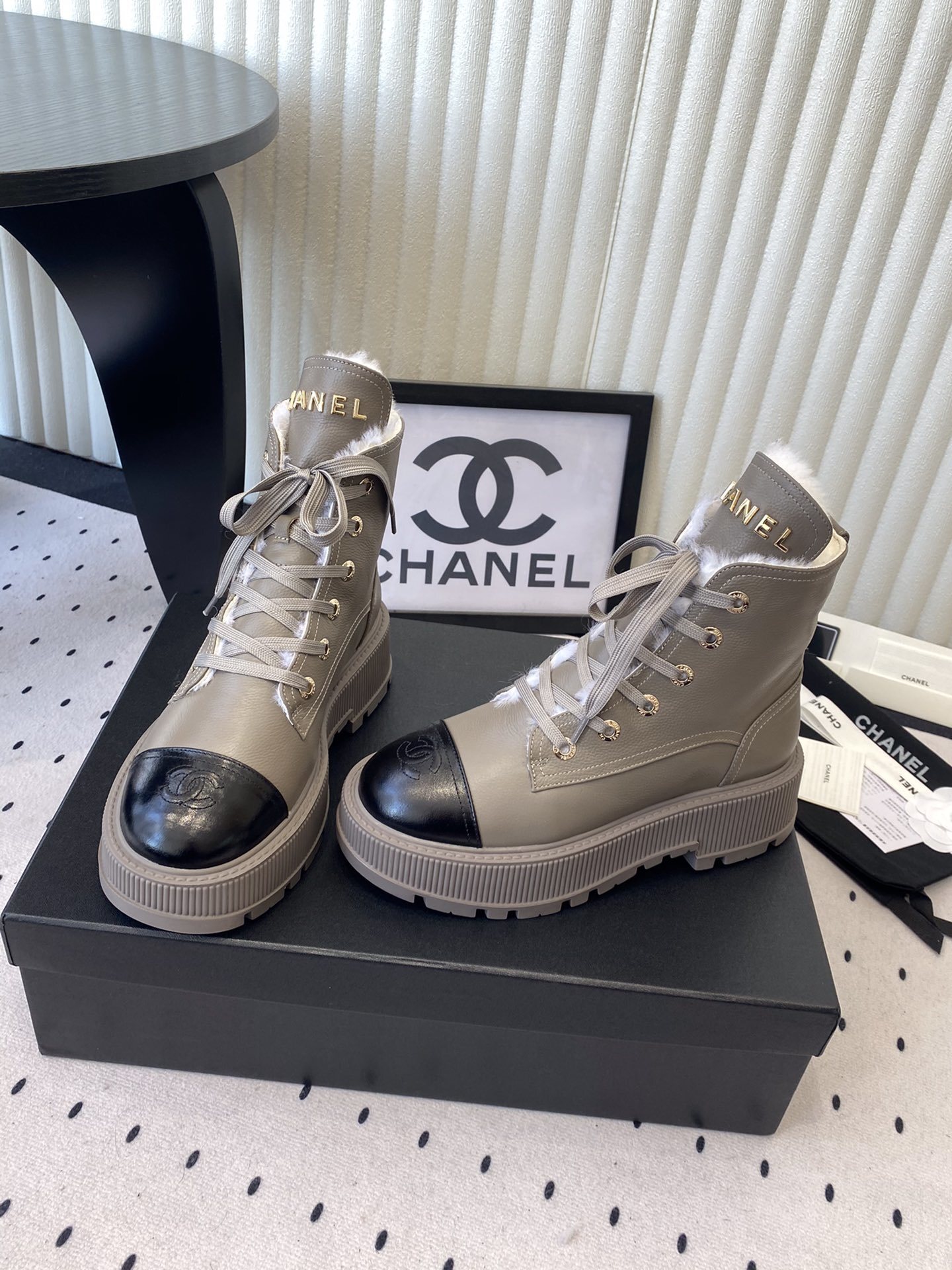 Chanel taupe leather lace-up boots with black patent toe caps and white shearling lining displayed on a black designer box - Hình 8