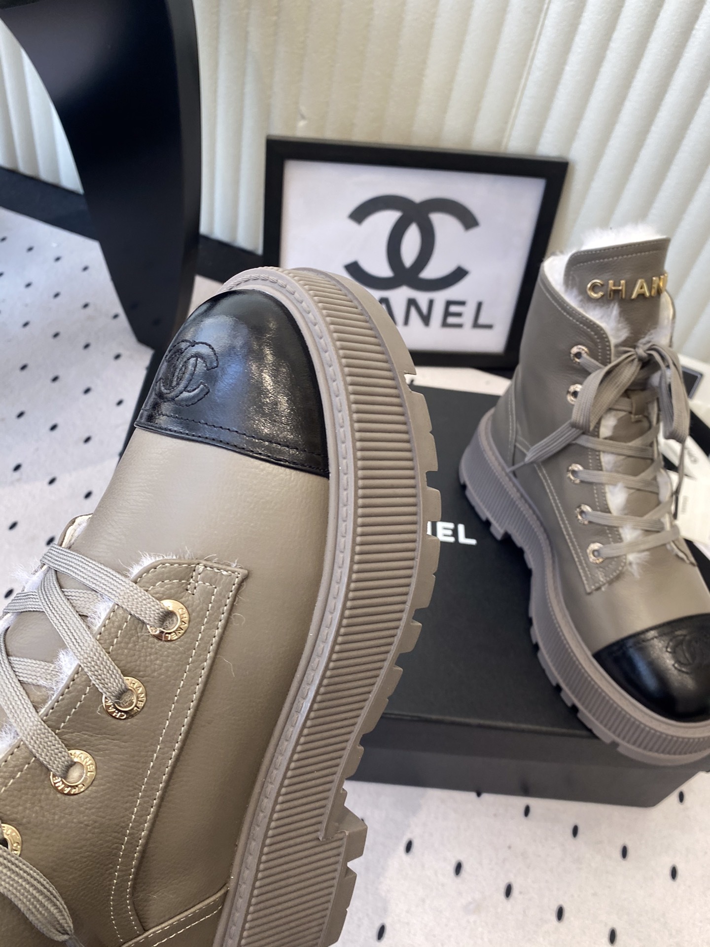Chanel taupe leather lace-up boots with black patent toe caps and white shearling lining displayed on a black designer box - Hình 6