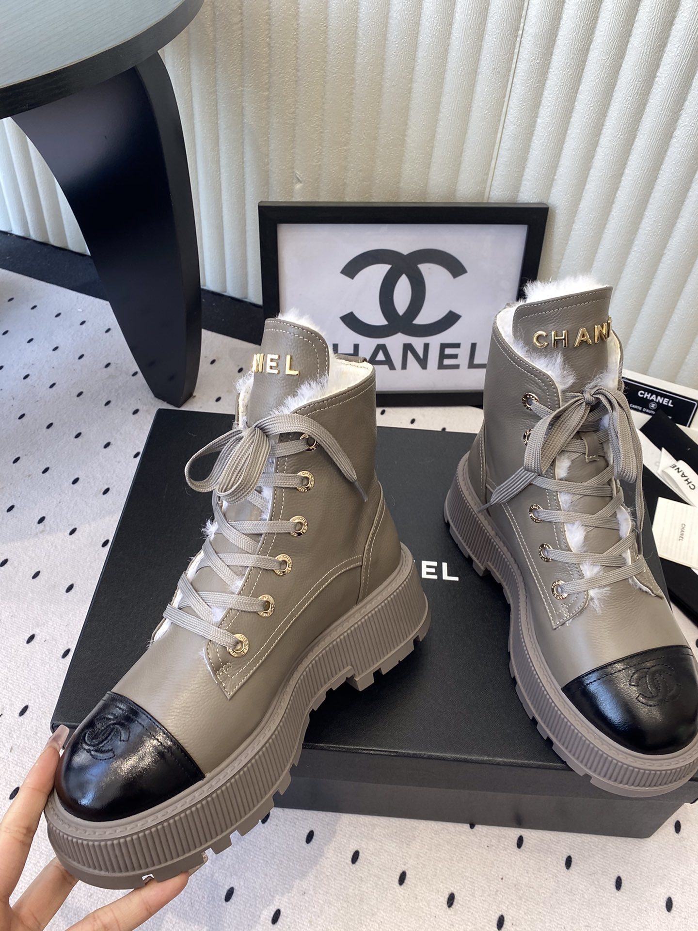 Chanel taupe leather lace-up boots with black patent toe caps and white shearling lining displayed on a black designer box - Hình 5