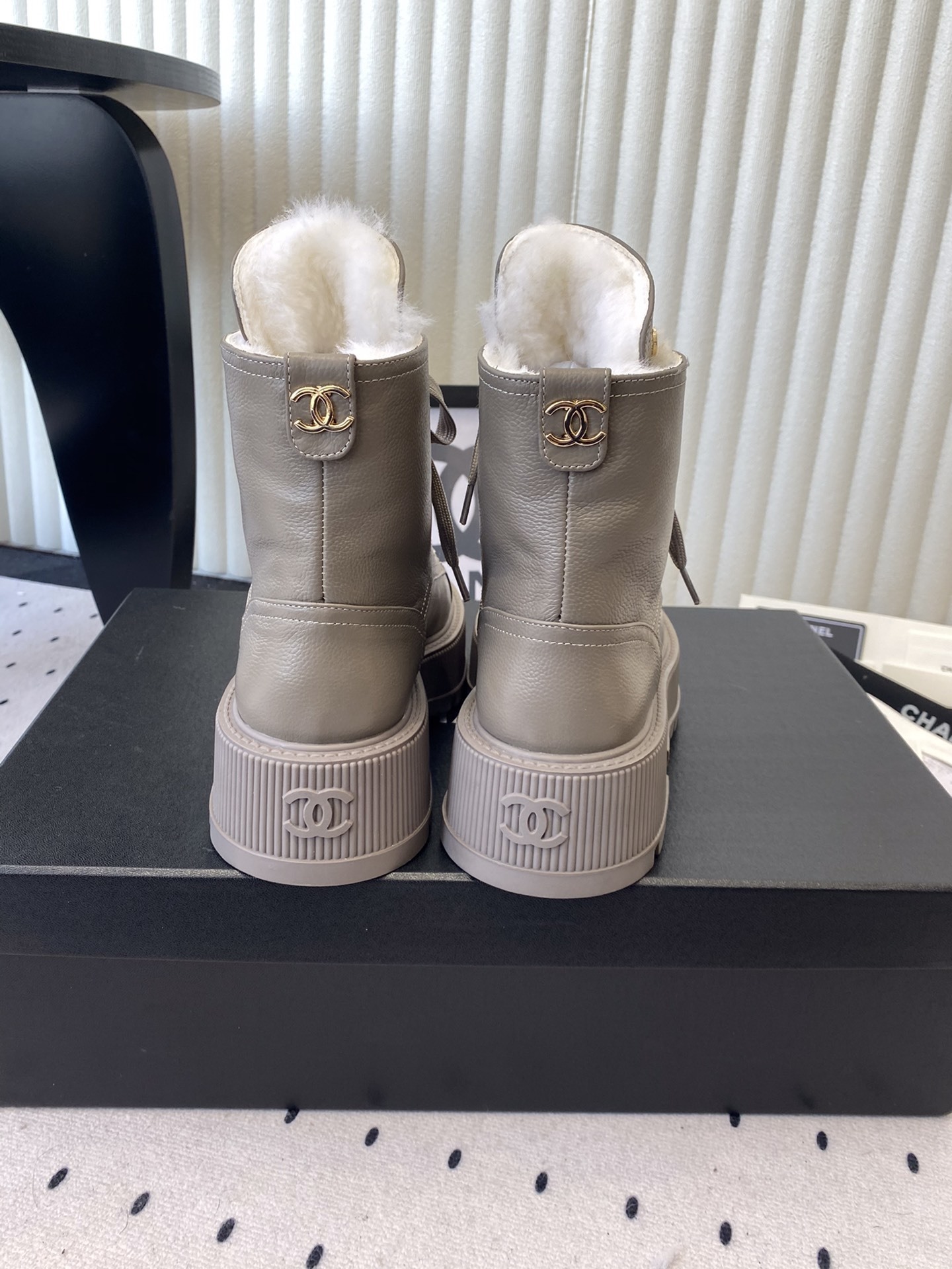 Chanel taupe leather lace-up boots with black patent toe caps and white shearling lining displayed on a black designer box - Hình 3