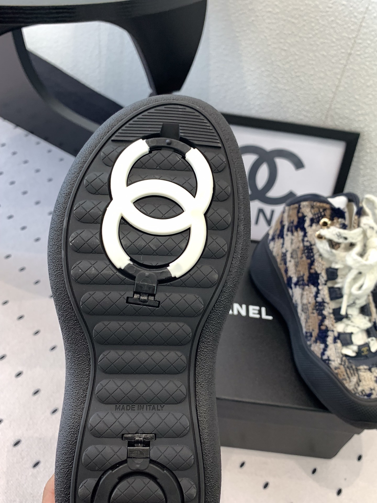 Pair of Chanel high-top sneakers in navy and beige tweed with chunky black rubber soles and thick white laces sitting on a black box. - Hình 9