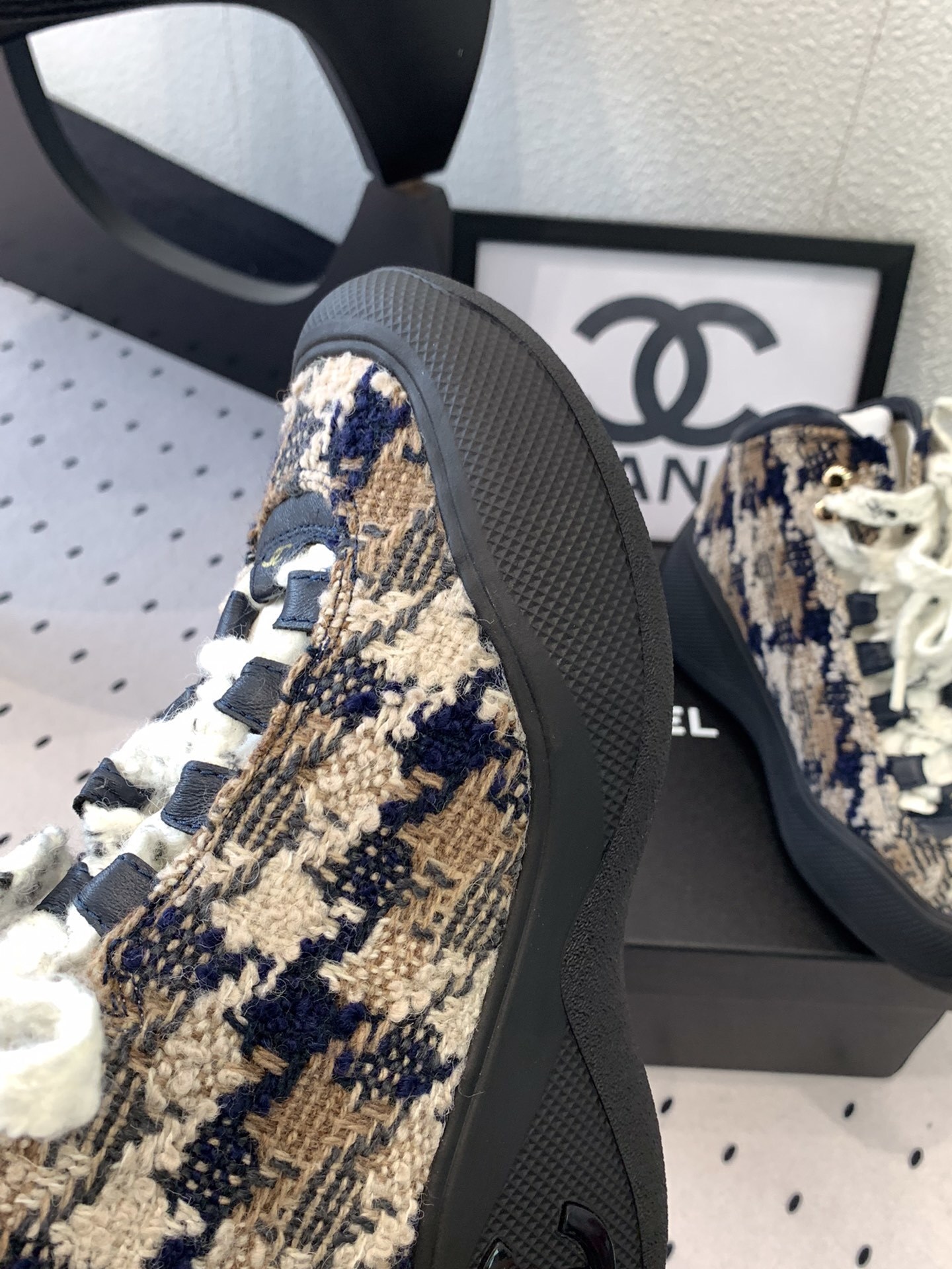 Pair of Chanel high-top sneakers in navy and beige tweed with chunky black rubber soles and thick white laces sitting on a black box. - Hình 7