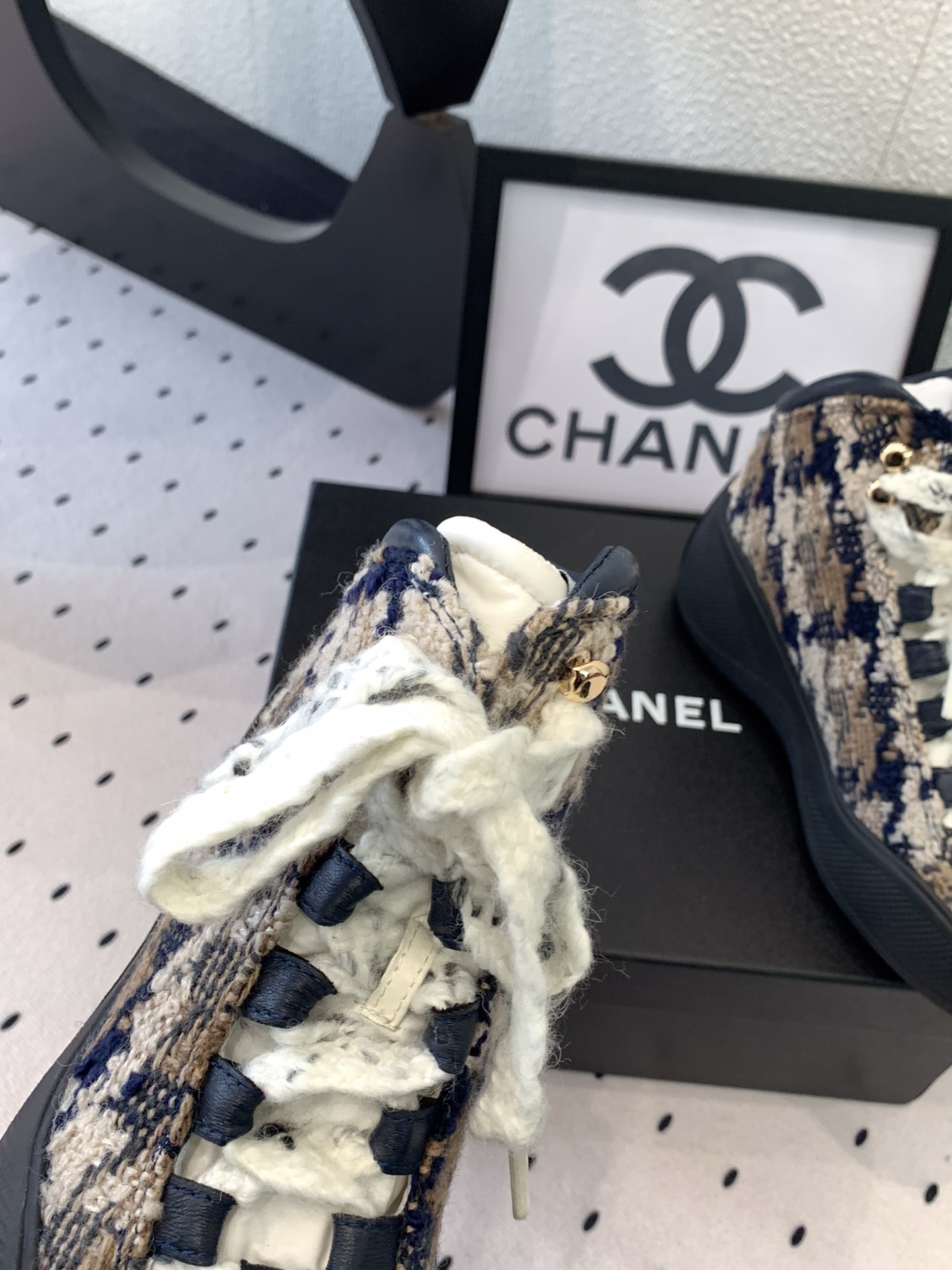 Pair of Chanel high-top sneakers in navy and beige tweed with chunky black rubber soles and thick white laces sitting on a black box. - Hình 6
