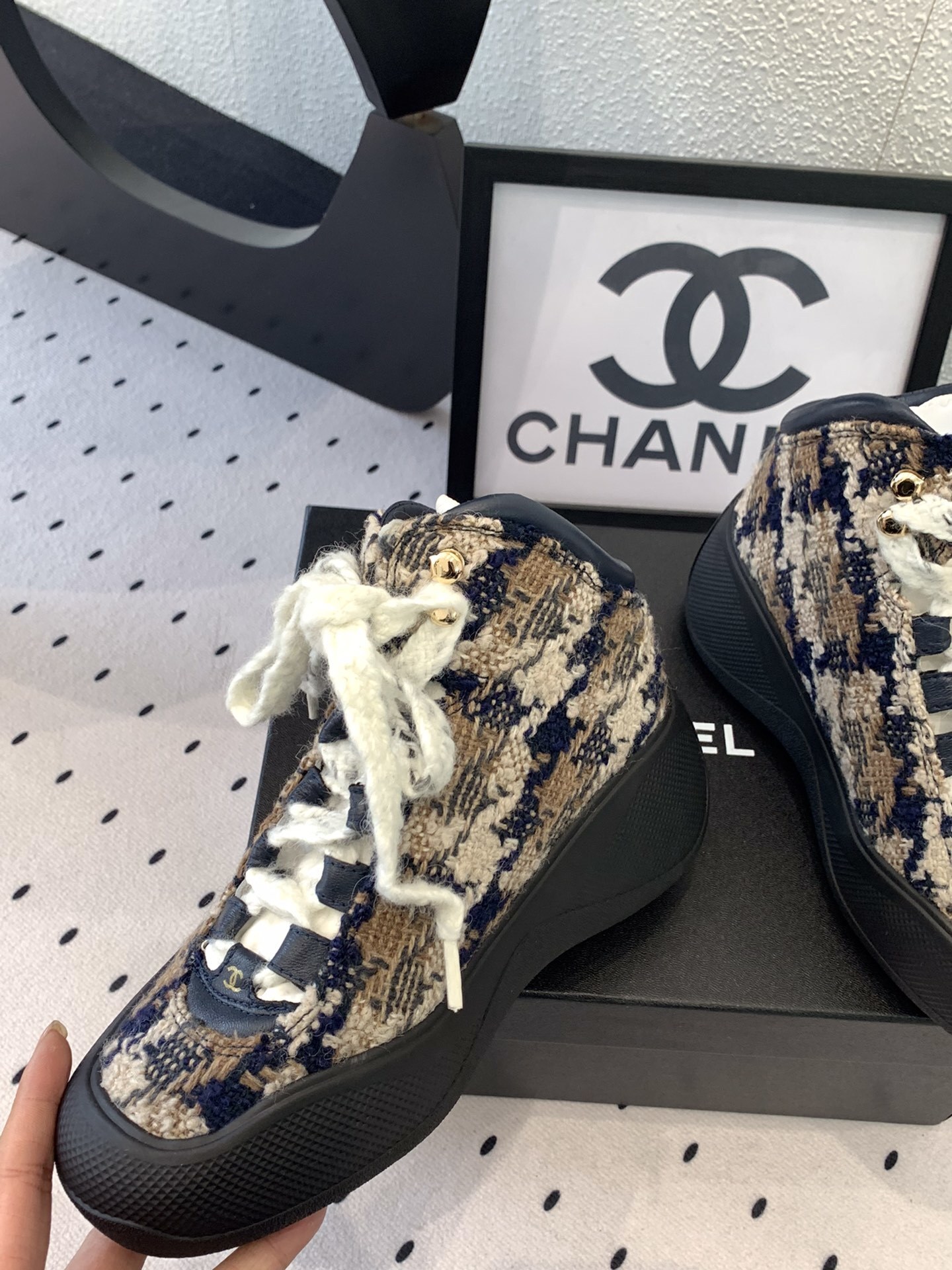 Pair of Chanel high-top sneakers in navy and beige tweed with chunky black rubber soles and thick white laces sitting on a black box. - Hình 5