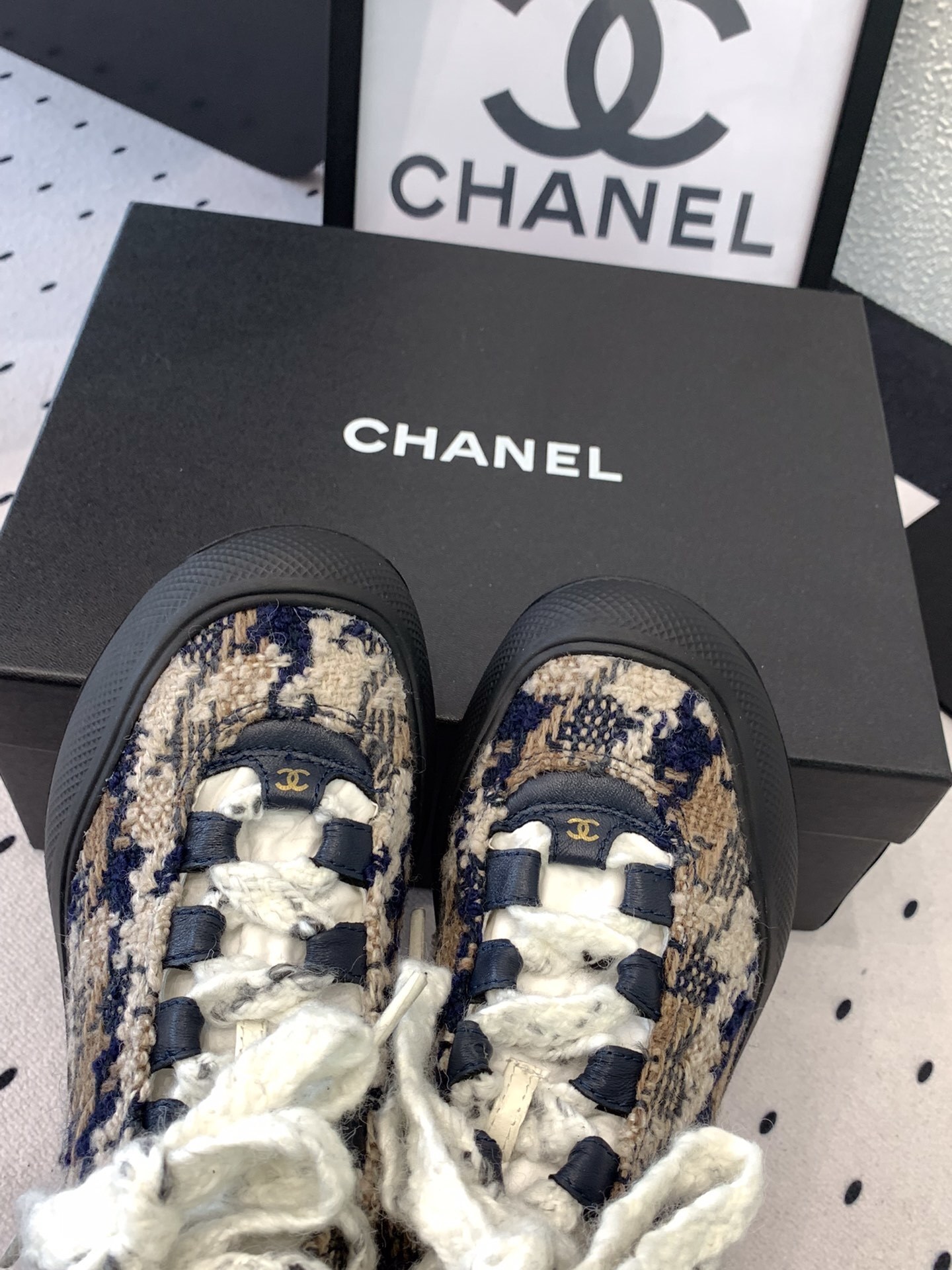 Pair of Chanel high-top sneakers in navy and beige tweed with chunky black rubber soles and thick white laces sitting on a black box. - Hình 4
