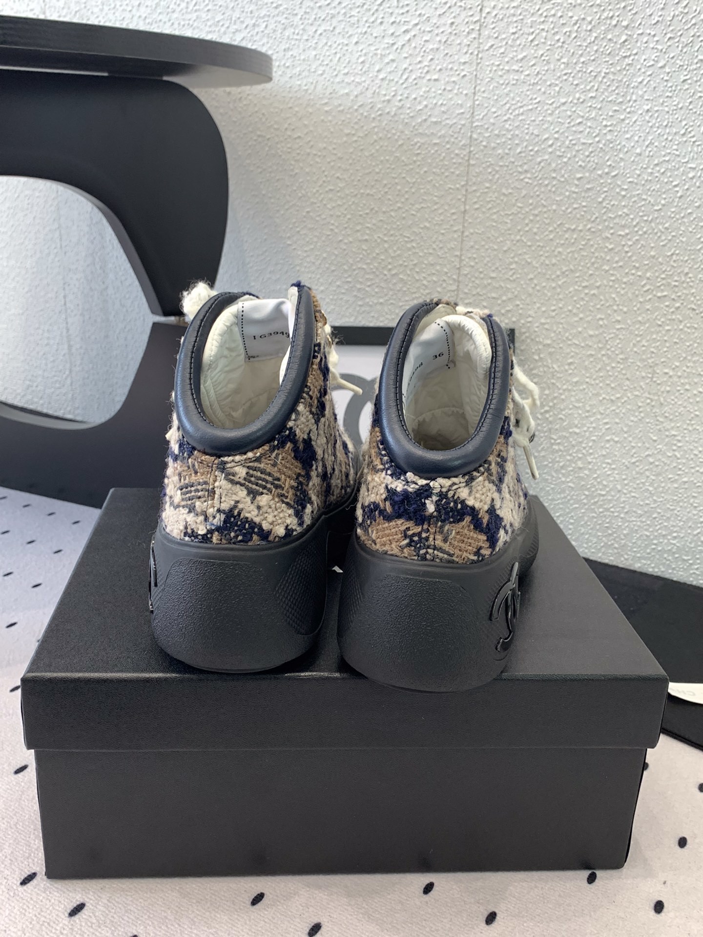 Pair of Chanel high-top sneakers in navy and beige tweed with chunky black rubber soles and thick white laces sitting on a black box. - Hình 3
