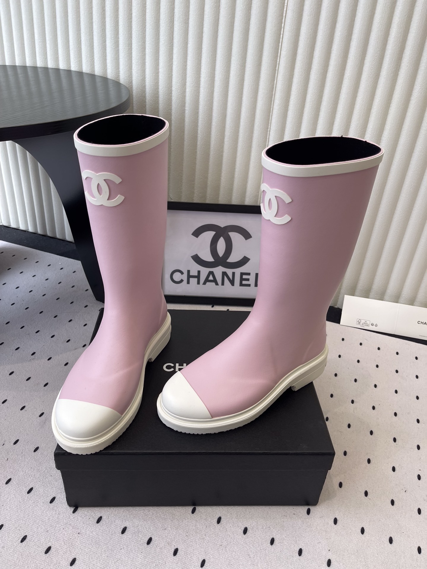 A pair of pastel pink rubber rain boots with white interlocking CC logo and white soles on a black designer box. - Hình 8