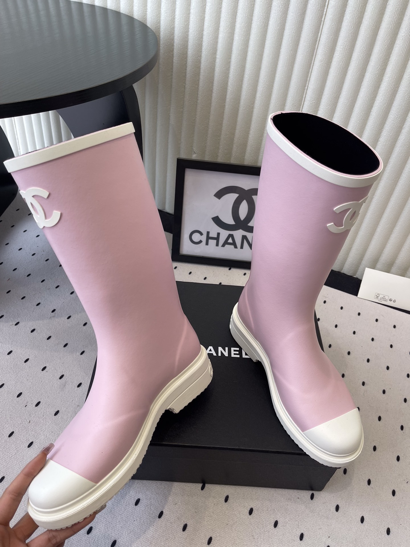 A pair of pastel pink rubber rain boots with white interlocking CC logo and white soles on a black designer box. - Hình 7