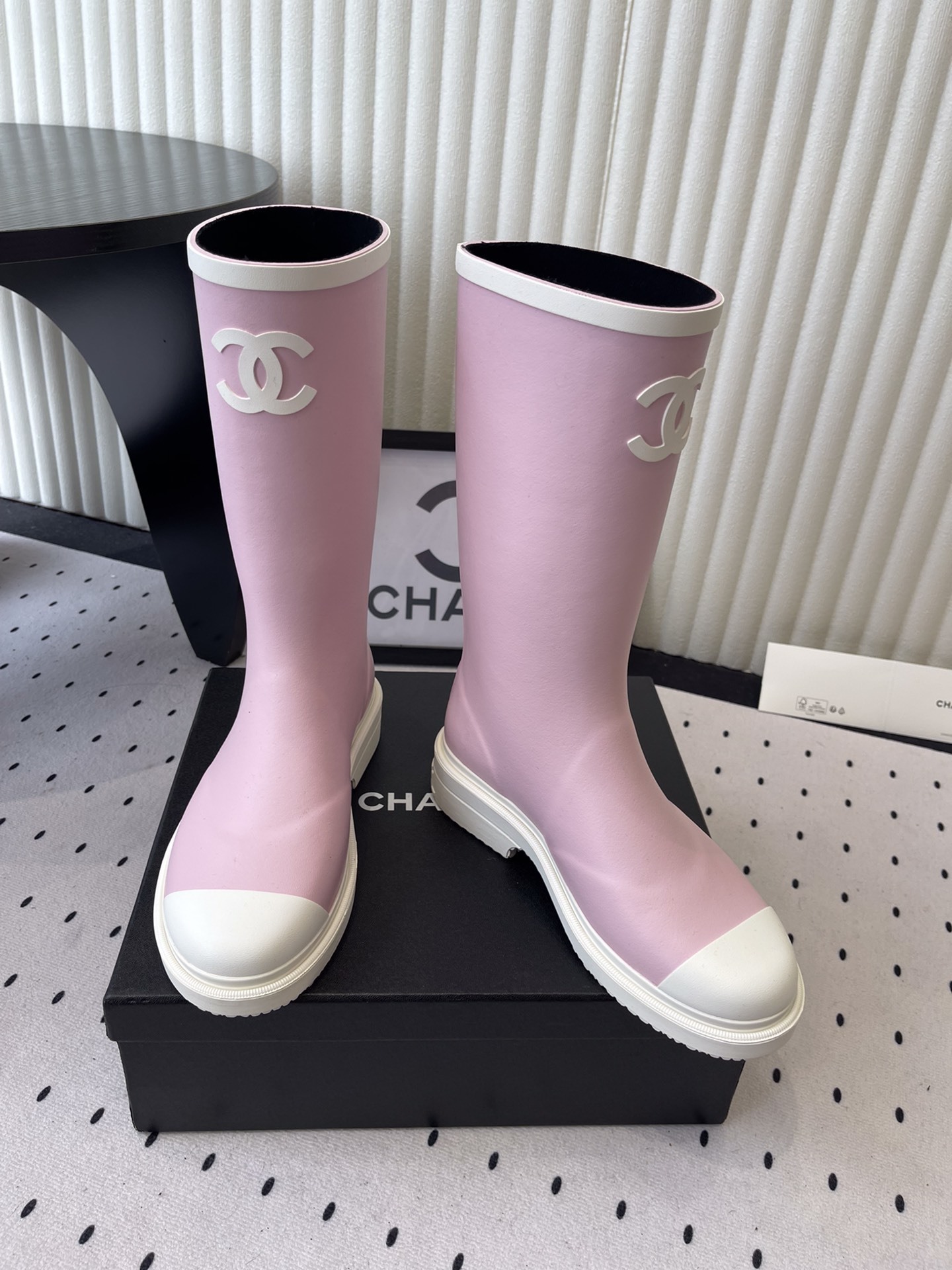 A pair of pastel pink rubber rain boots with white interlocking CC logo and white soles on a black designer box. - Hình 6
