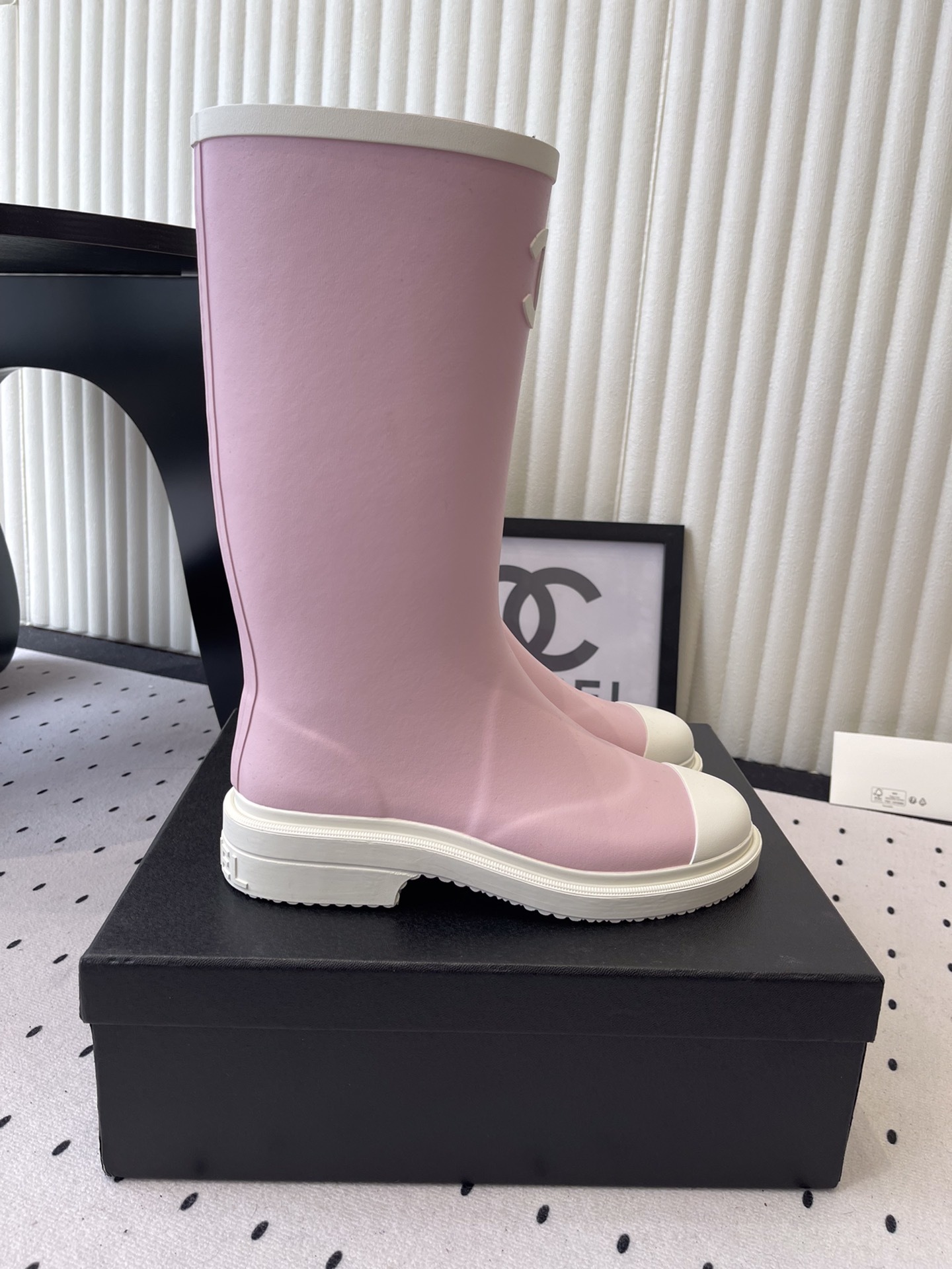 A pair of pastel pink rubber rain boots with white interlocking CC logo and white soles on a black designer box. - Hình 2