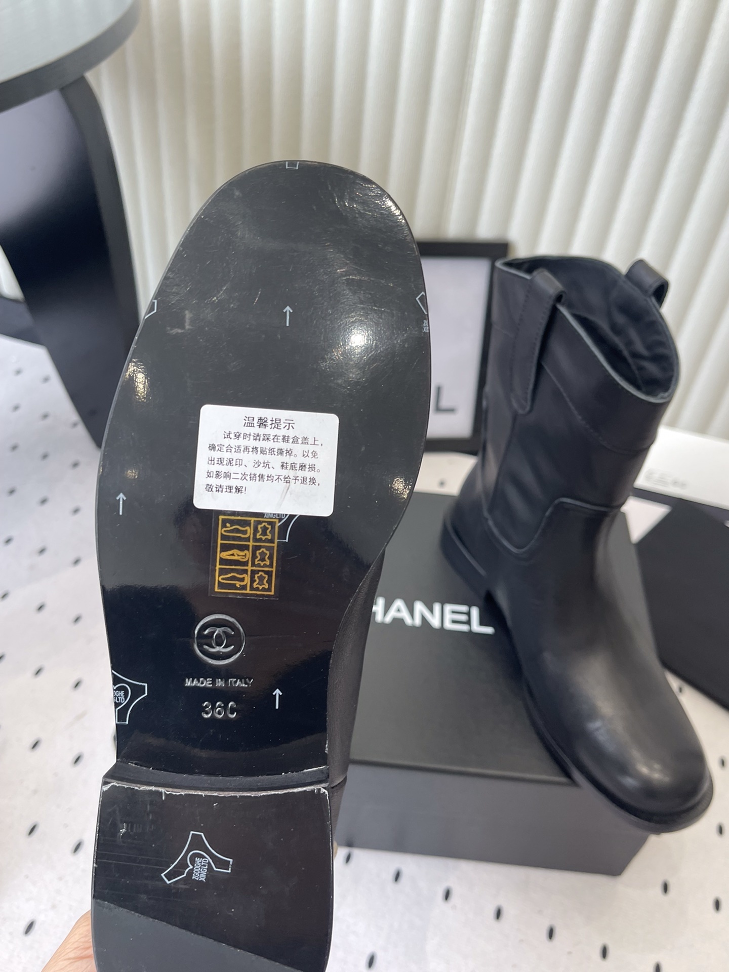A pair of Chanel black leather mid-calf biker boots with white logo pull tabs displayed on a black Chanel shoe box. - Hình 9