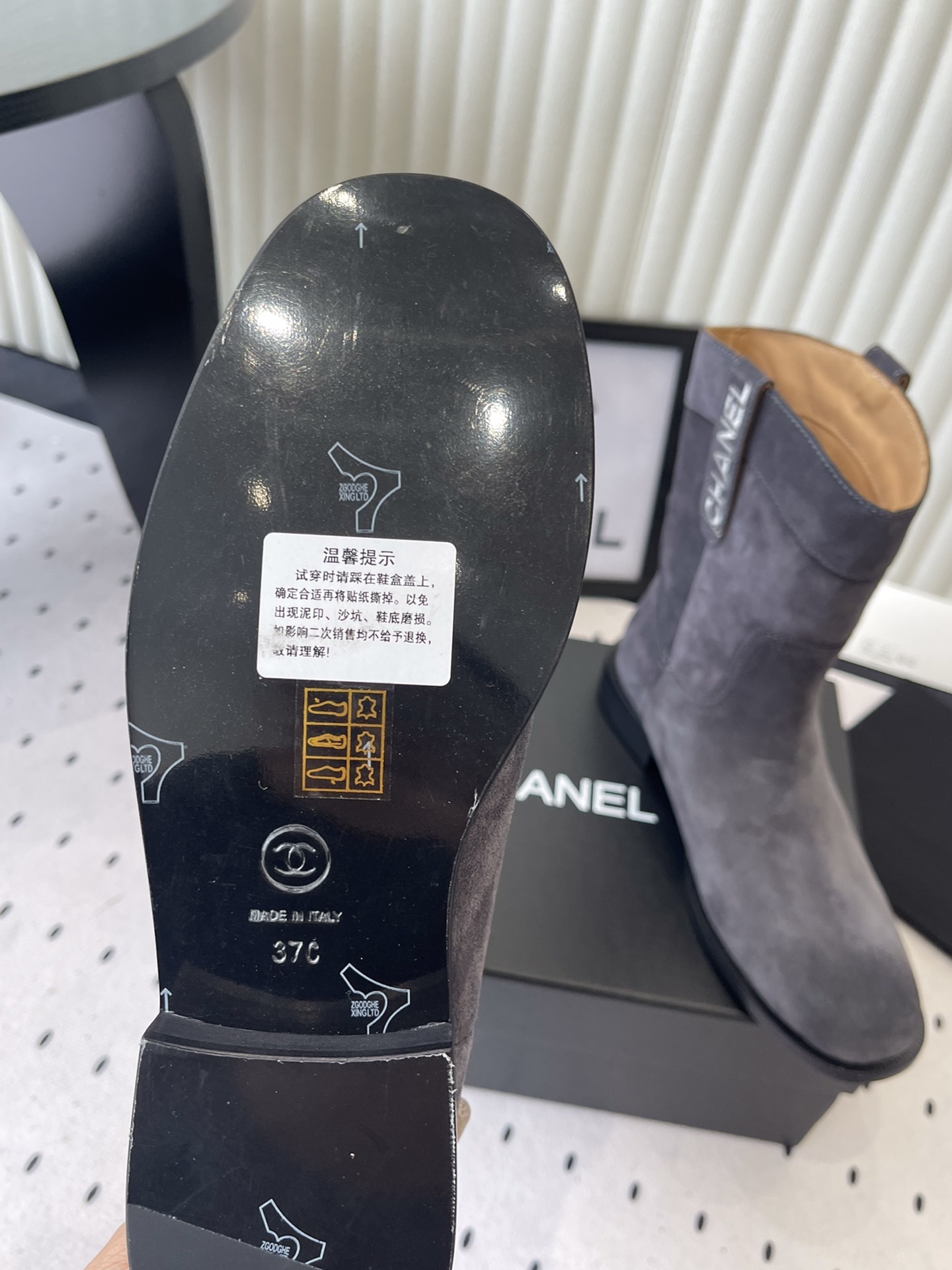 A pair of luxury Chanel gray suede mid-calf boots with logo pull tabs displayed on a black box - Hình 9