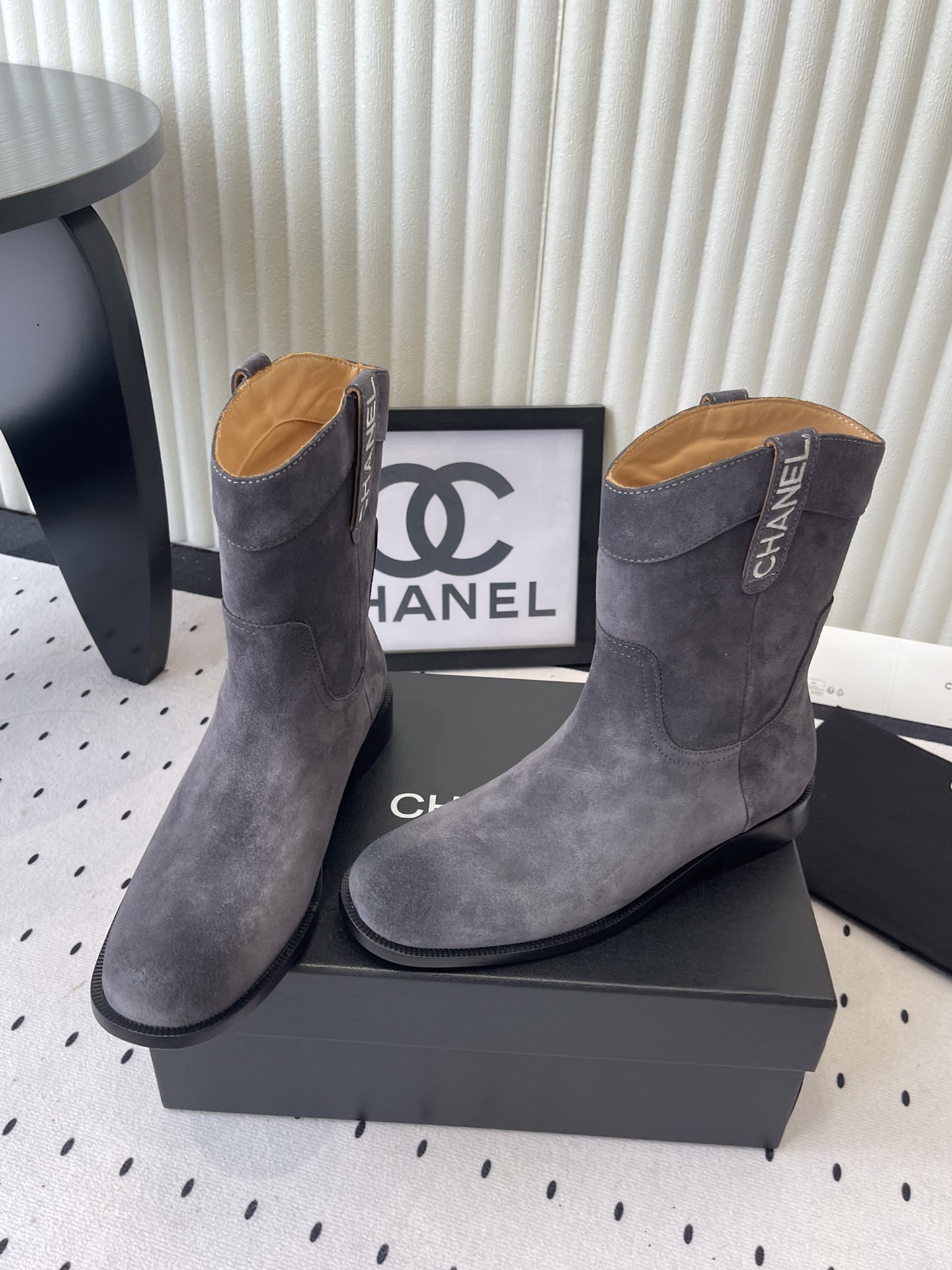 A pair of luxury Chanel gray suede mid-calf boots with logo pull tabs displayed on a black box - Hình 8