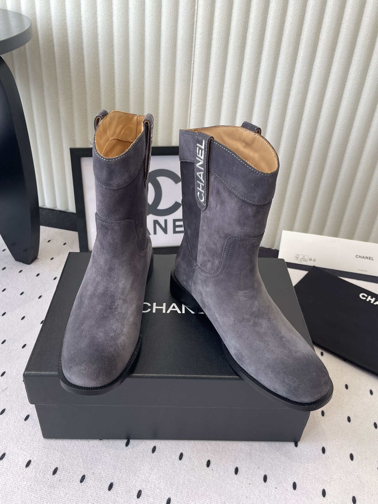 A pair of luxury Chanel gray suede mid-calf boots with logo pull tabs displayed on a black box - Hình 7