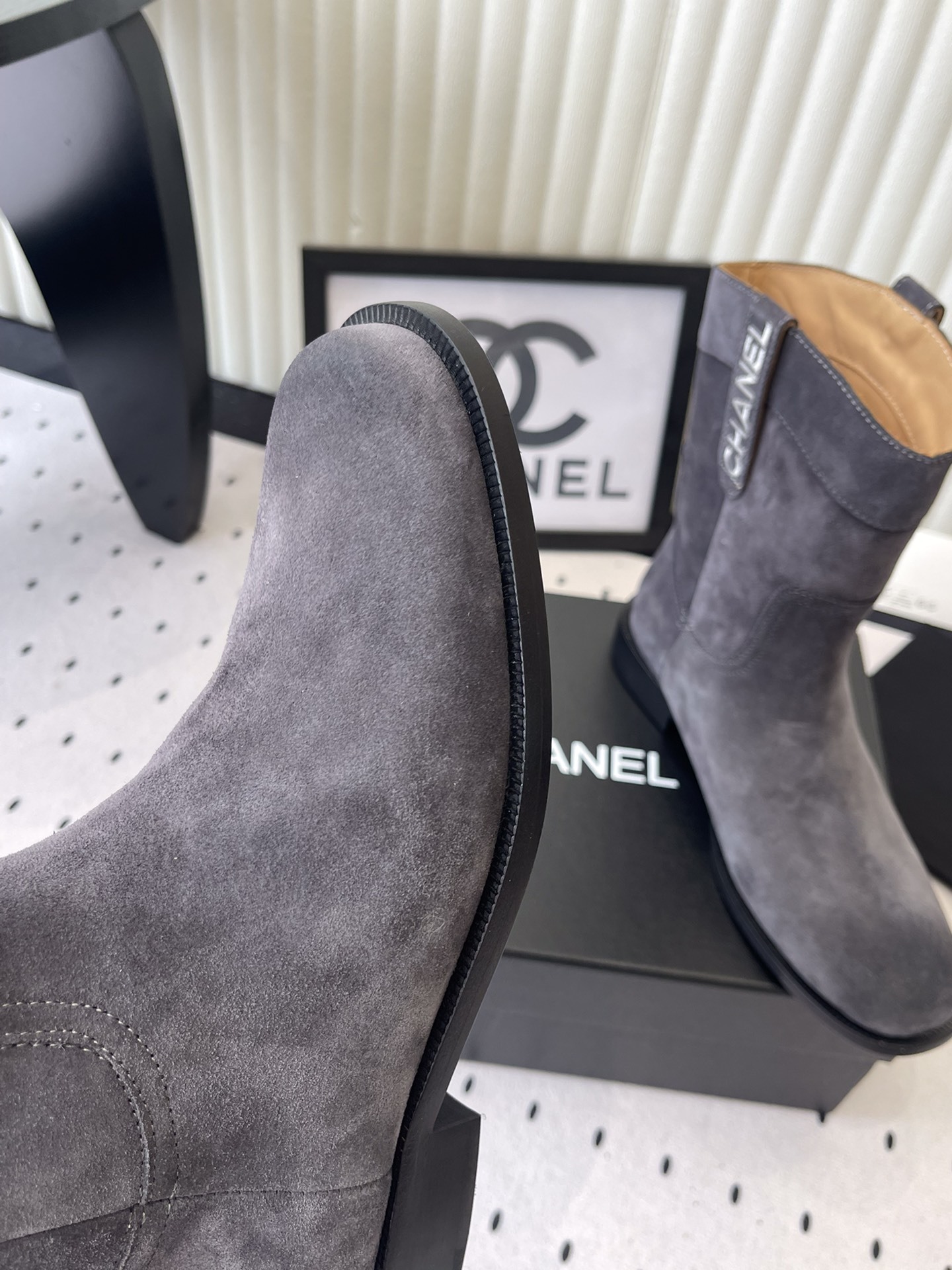 A pair of luxury Chanel gray suede mid-calf boots with logo pull tabs displayed on a black box - Hình 6