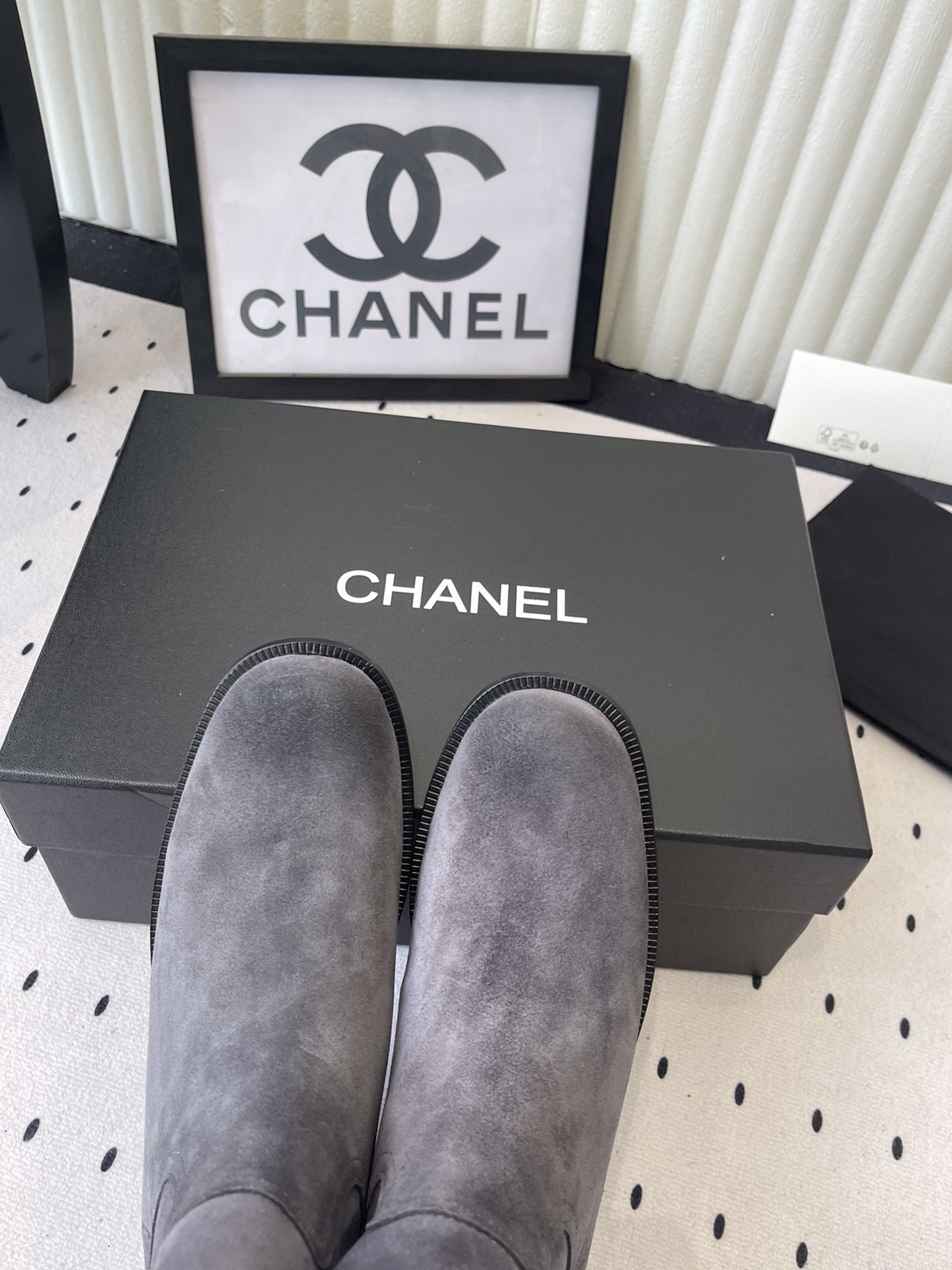 A pair of luxury Chanel gray suede mid-calf boots with logo pull tabs displayed on a black box - Hình 4