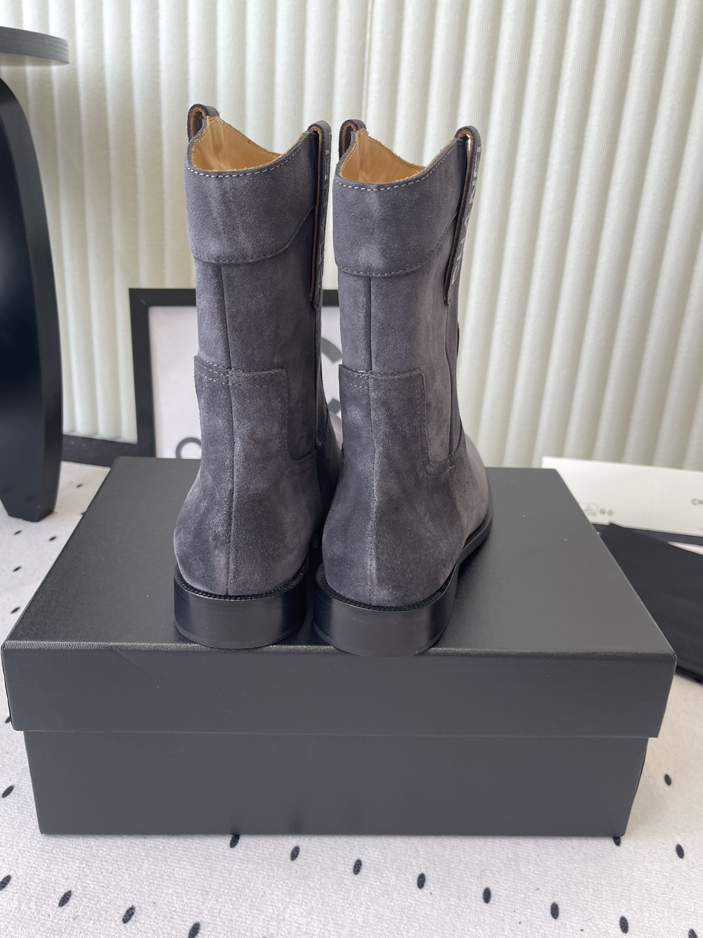 A pair of luxury Chanel gray suede mid-calf boots with logo pull tabs displayed on a black box - Hình 3
