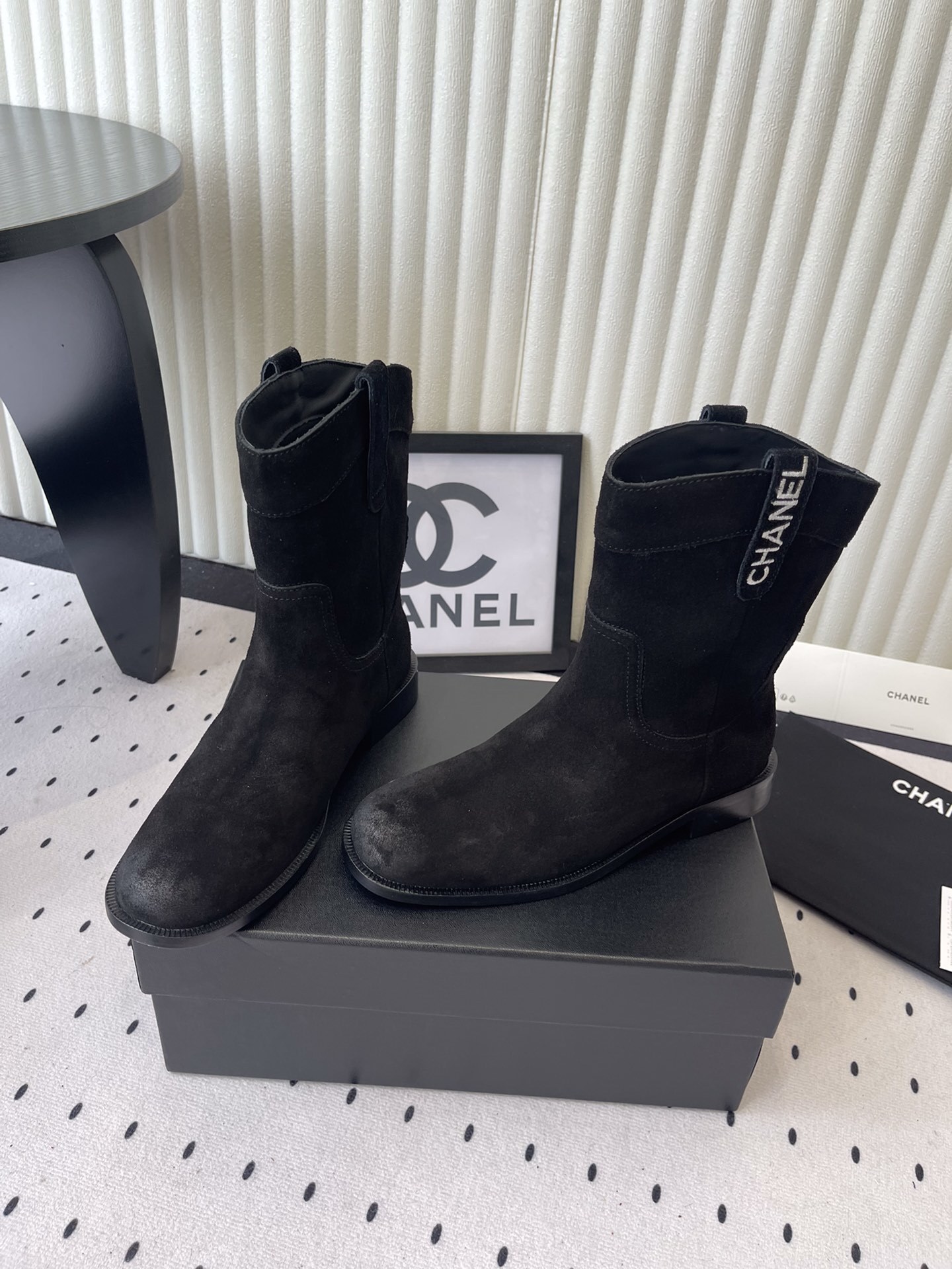 Pair of Chanel black suede mid-calf boots with white logo pull tabs displayed on a black Chanel shoe box - Hình 8