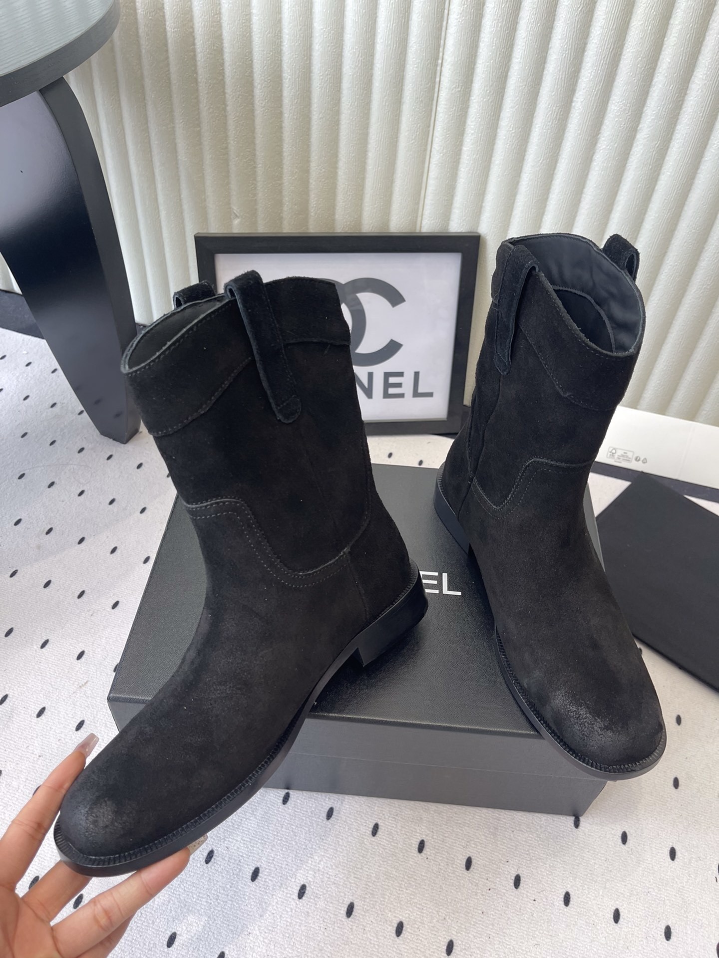 Pair of Chanel black suede mid-calf boots with white logo pull tabs displayed on a black Chanel shoe box - Hình 5