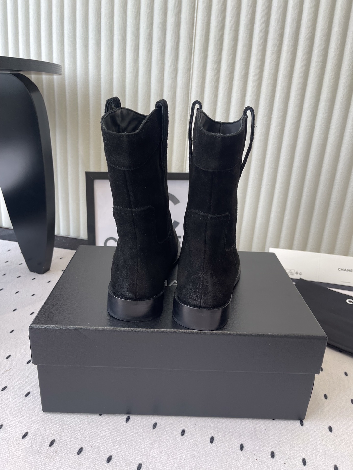 Pair of Chanel black suede mid-calf boots with white logo pull tabs displayed on a black Chanel shoe box - Hình 3